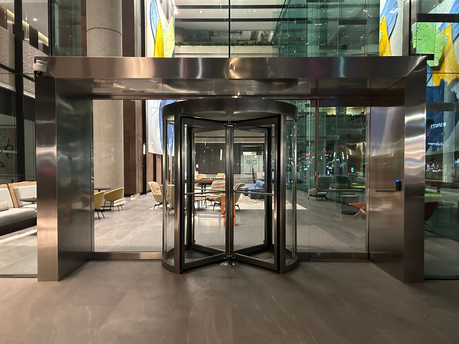 Turnstile entrance to a modern building with glass doors and a reflective steel frame.