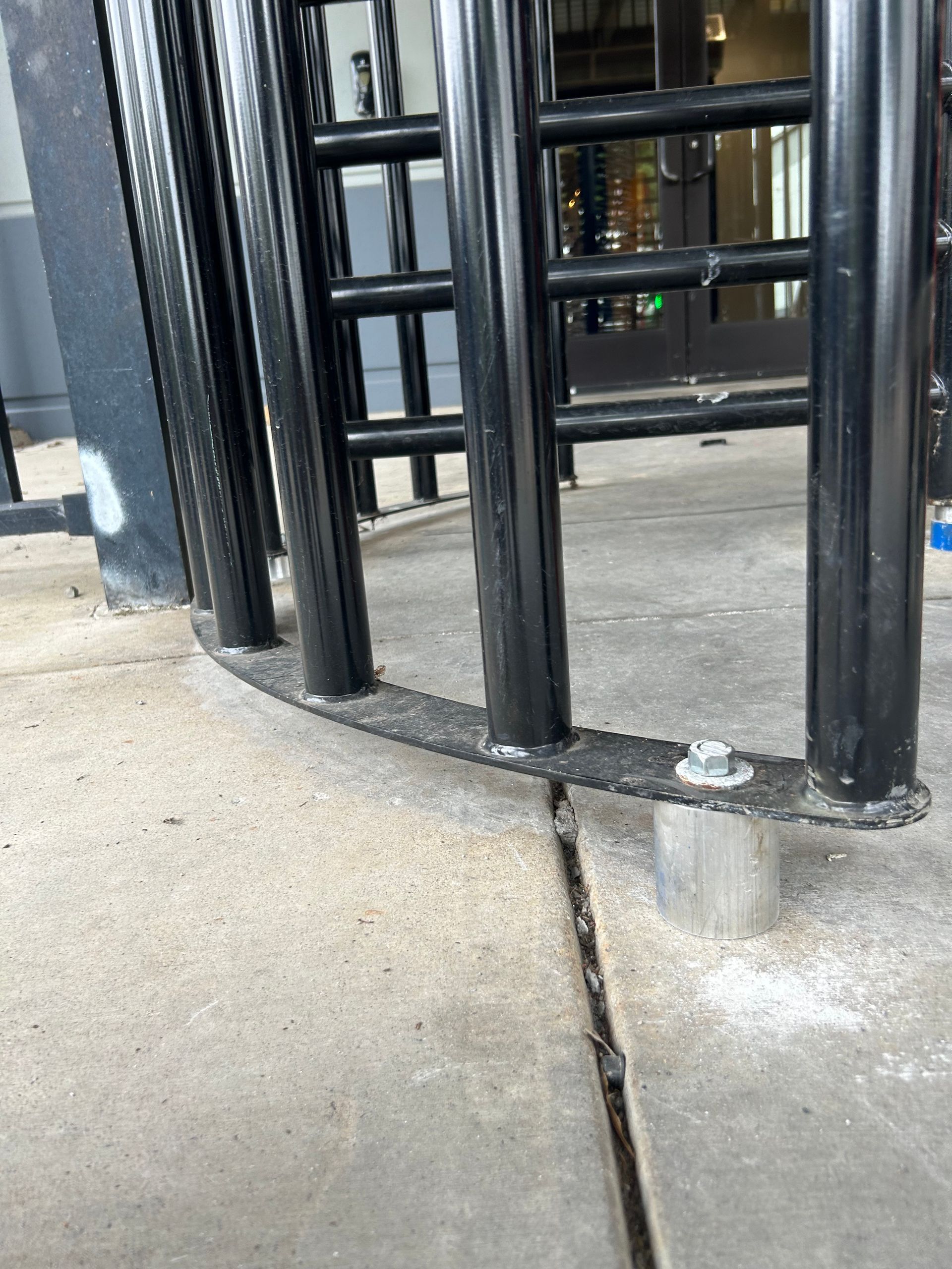 Black metal turnstile on a concrete surface, mounted to the ground with bolts.