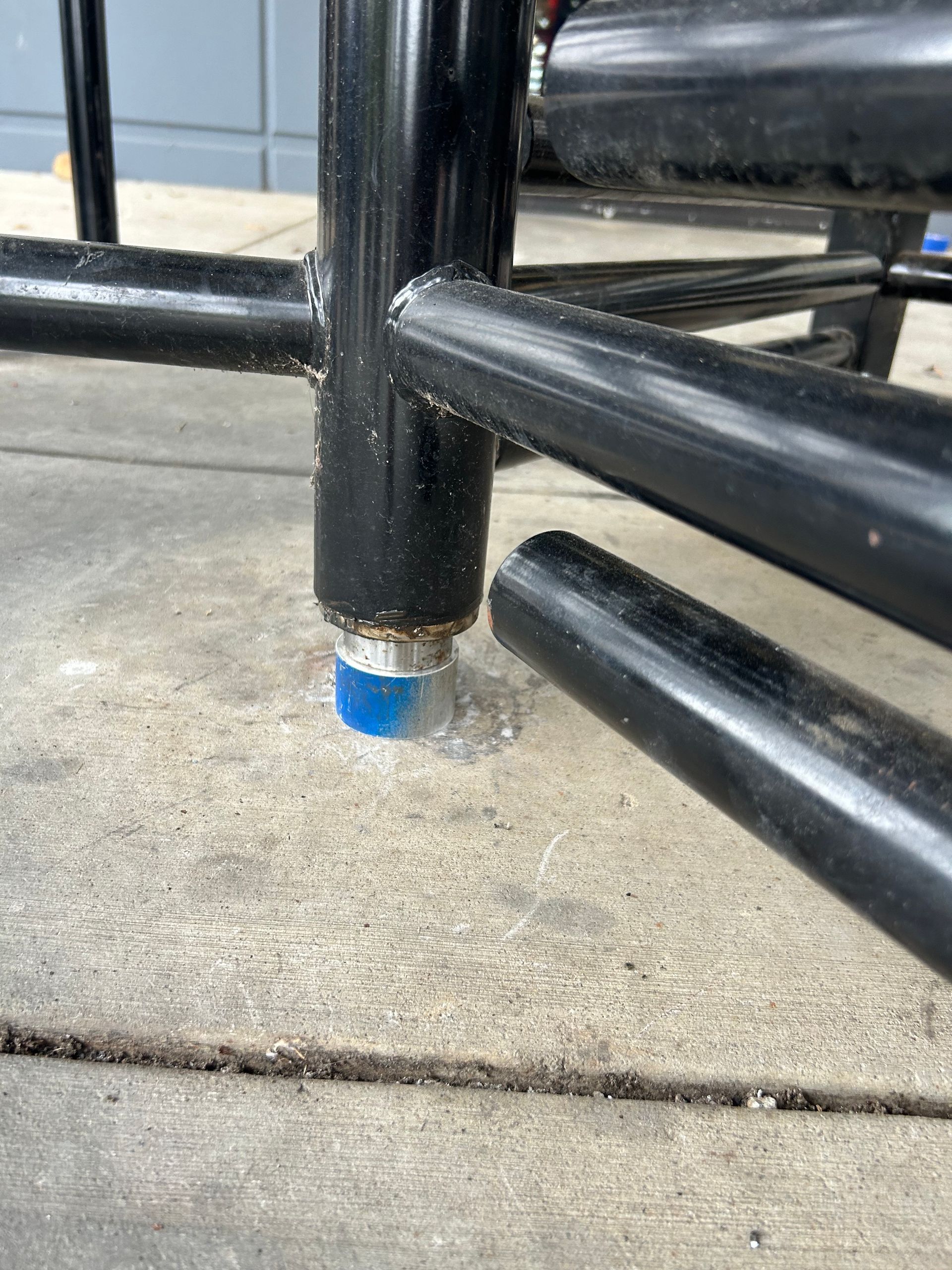 Black metal chair leg with a blue foot protector on a concrete surface.