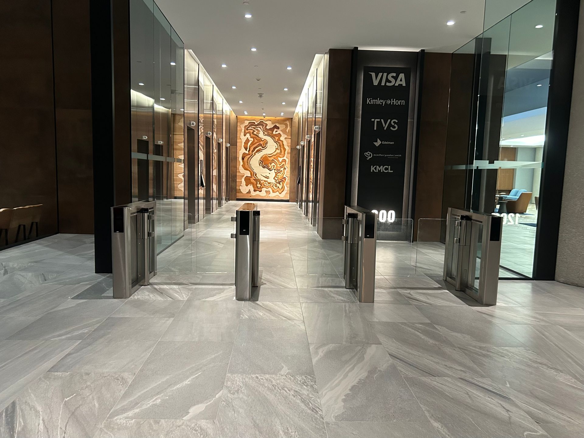 Entrance hallway with security turnstiles, signs for Visa and TVS, and a decorative panel.