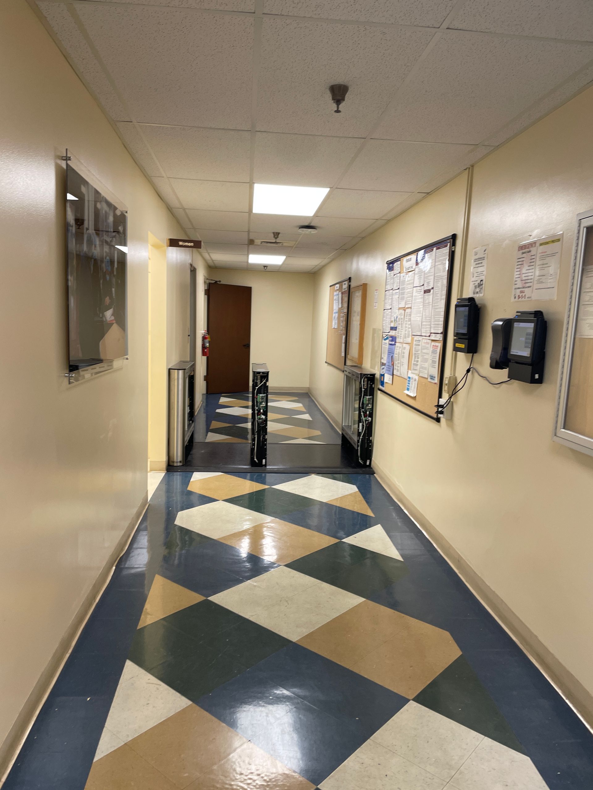 Long hallway with patterned floor, bulletin boards, and a door at the end.