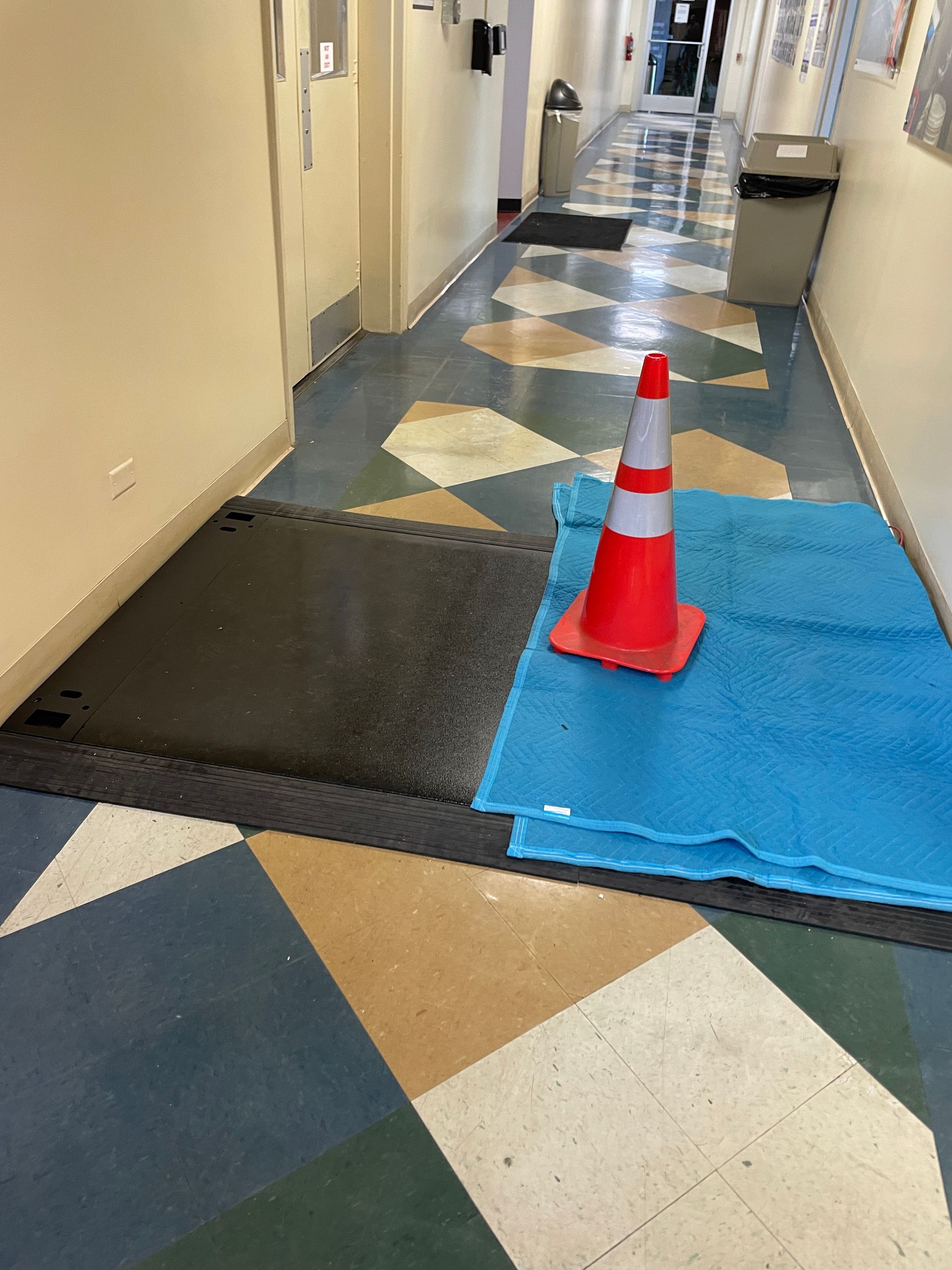 Hallway with water on floor, a traffic cone and blue absorbent pads.