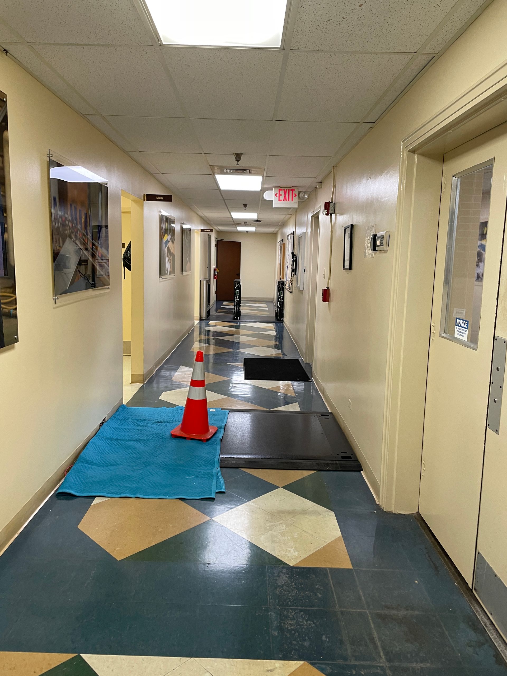 Hallway with blue, tan, and white patterned floor; a blue rug and orange traffic cone on the floor.