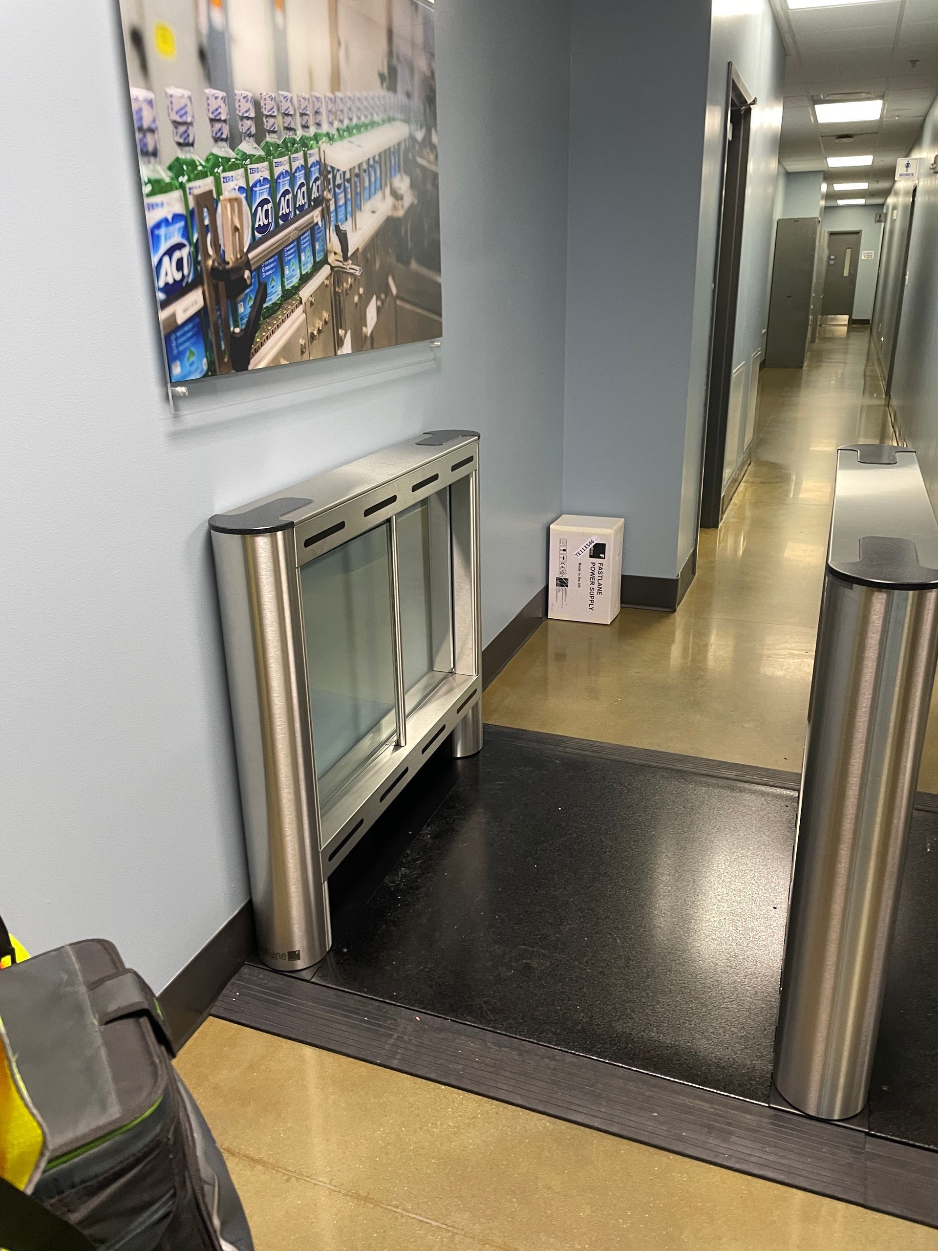 A hallway with turnstiles and security entrance; a picture hangs on the wall, a small white box is next to the wall.
