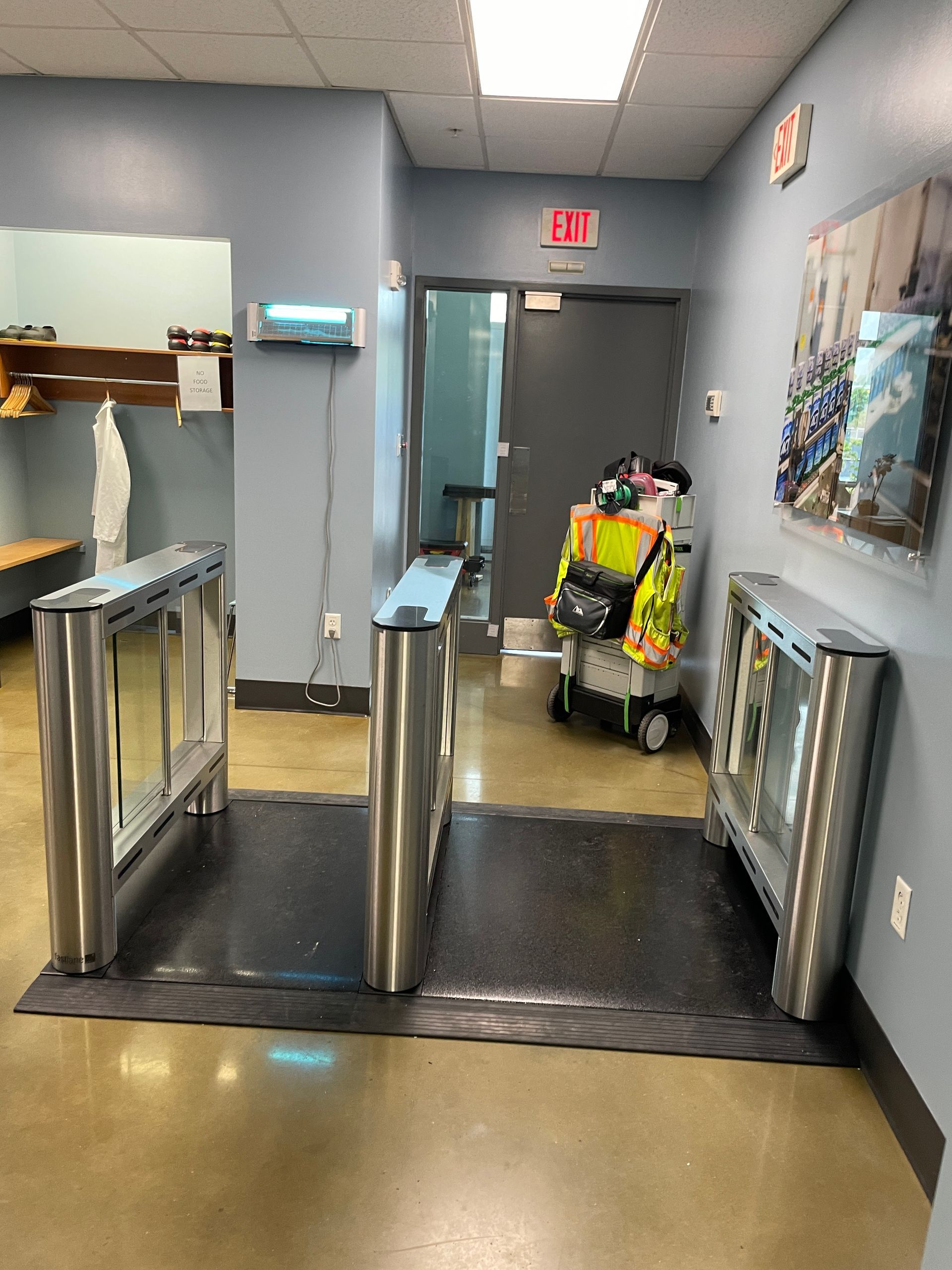 Hallway with turnstiles, a cleaning cart, and an exit sign.