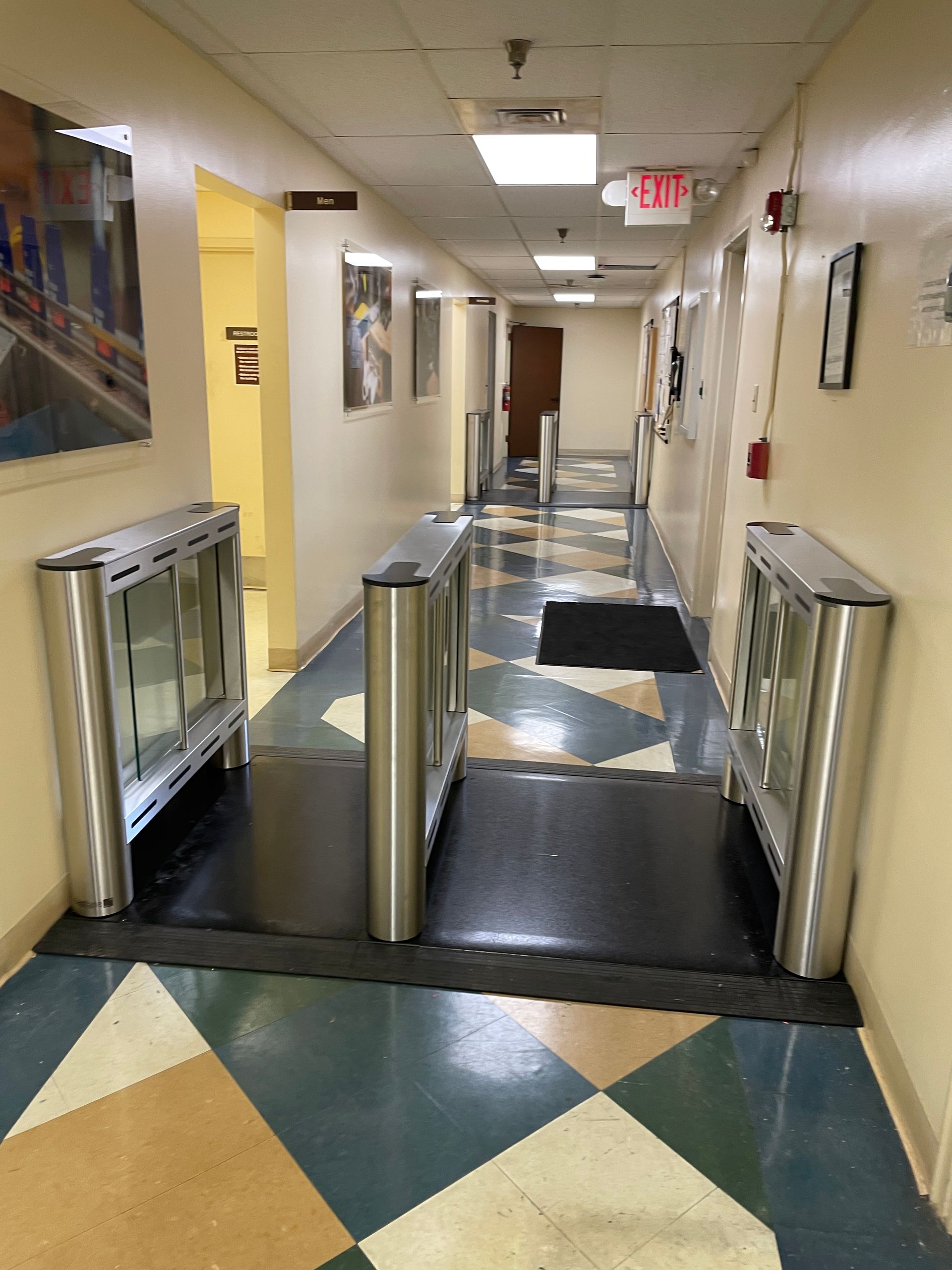 Hallway with security turnstiles and blue, cream, and brown tiled floor.