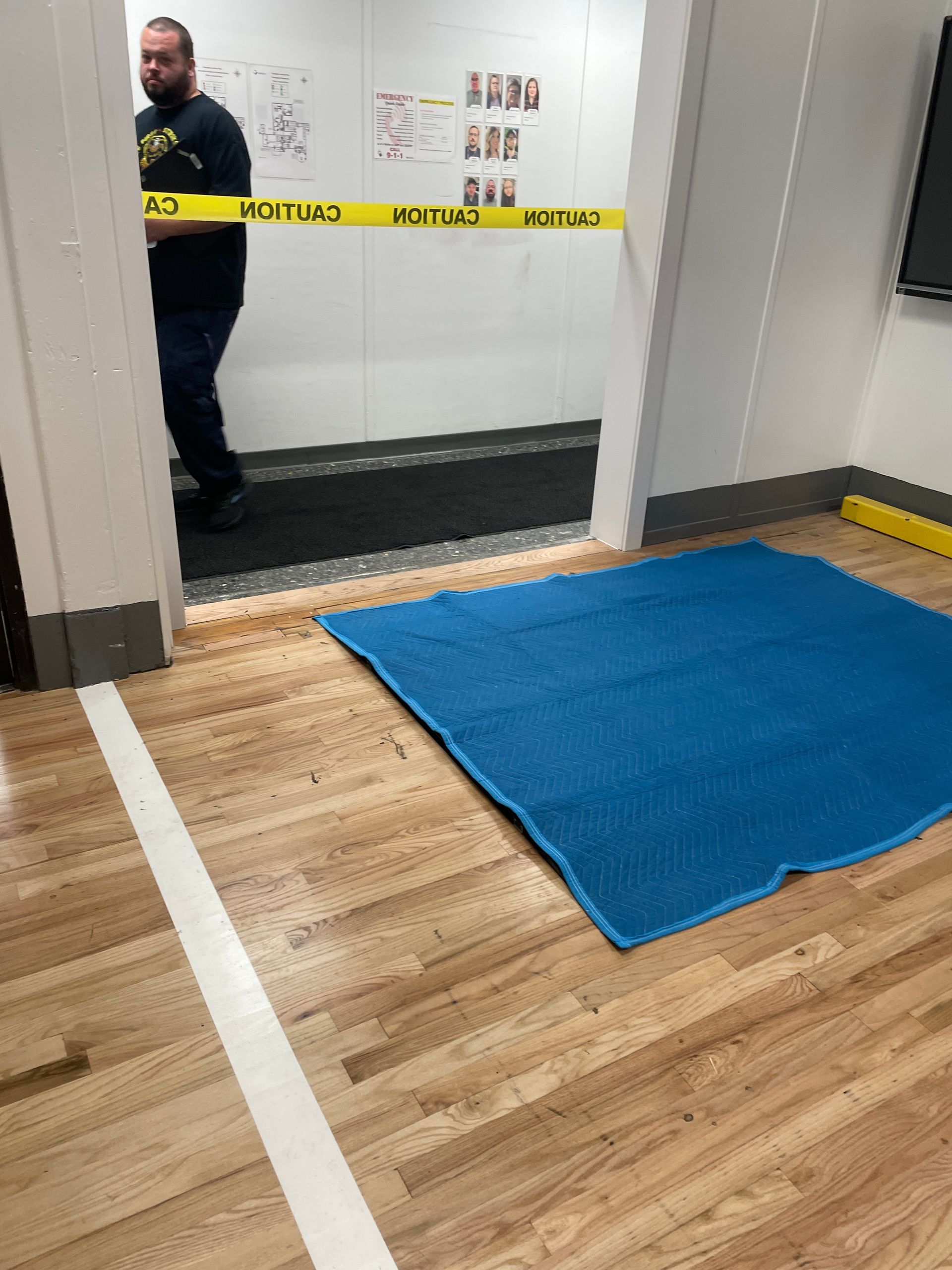 Person in doorway behind caution tape; blue mat on wooden floor in front.