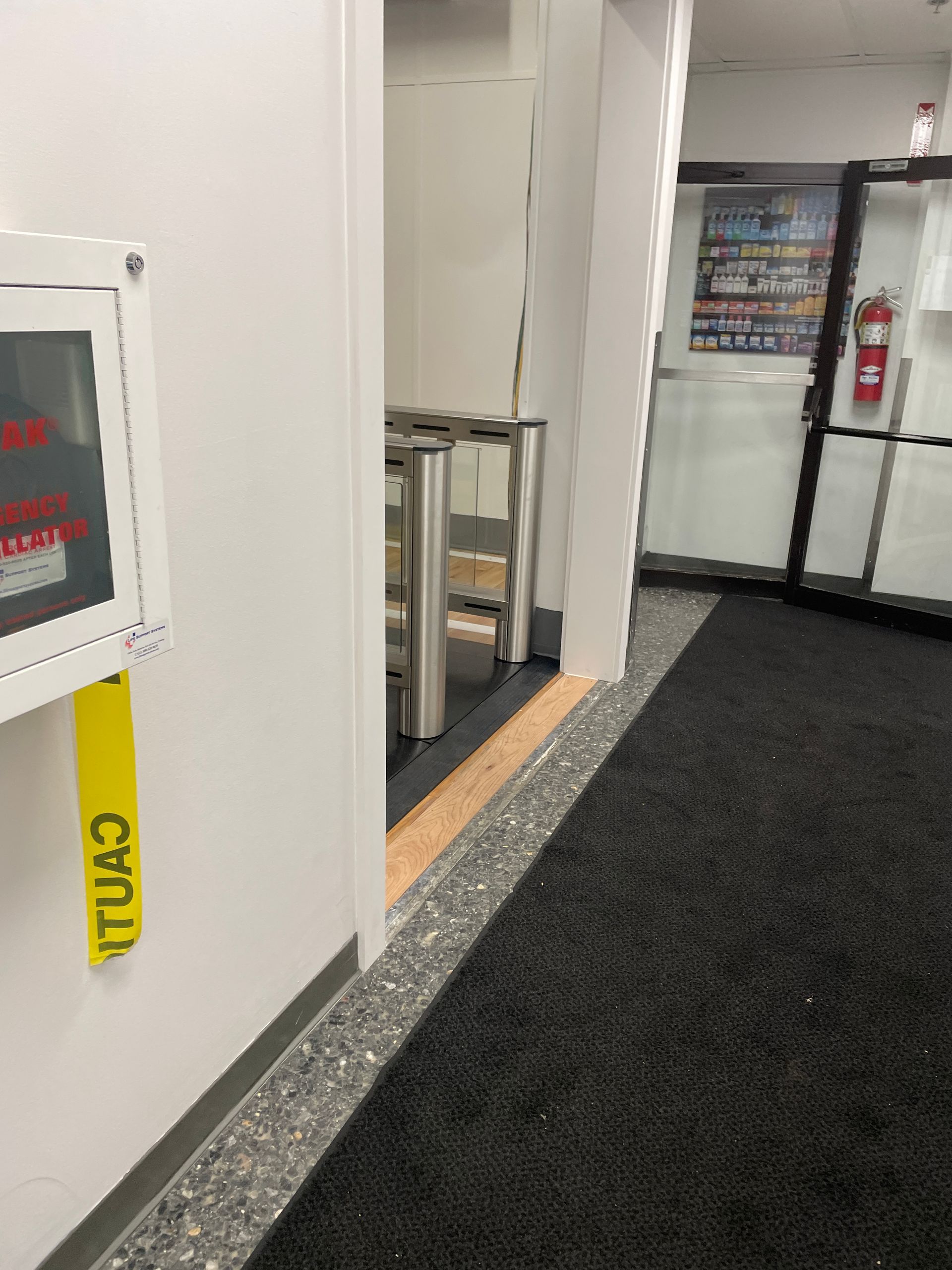 Hallway with a doorway, security turnstiles, and an exit door with a fire extinguisher. 