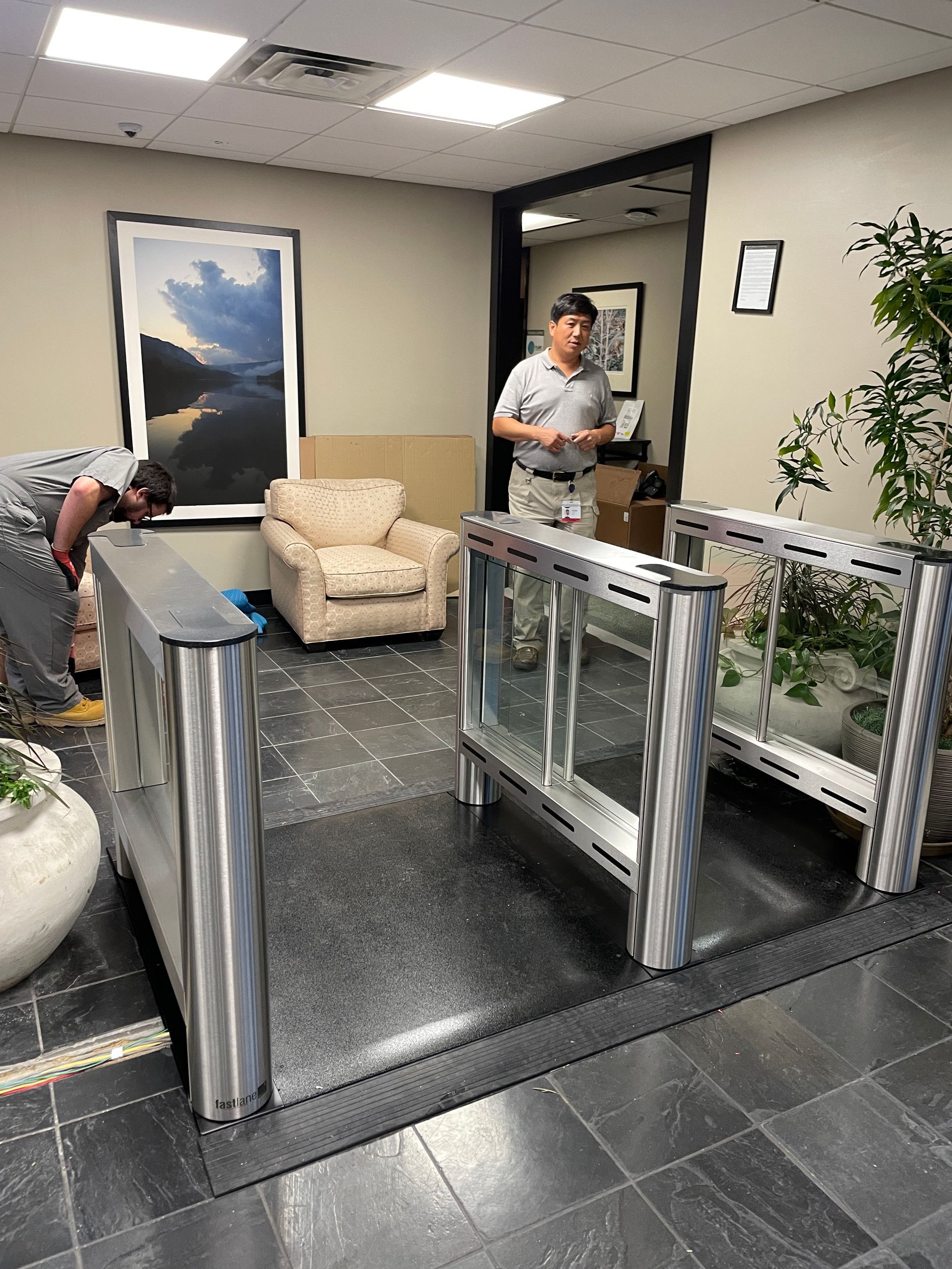 Turnstile entrance with two people; one man standing, the other leaning by furniture.
