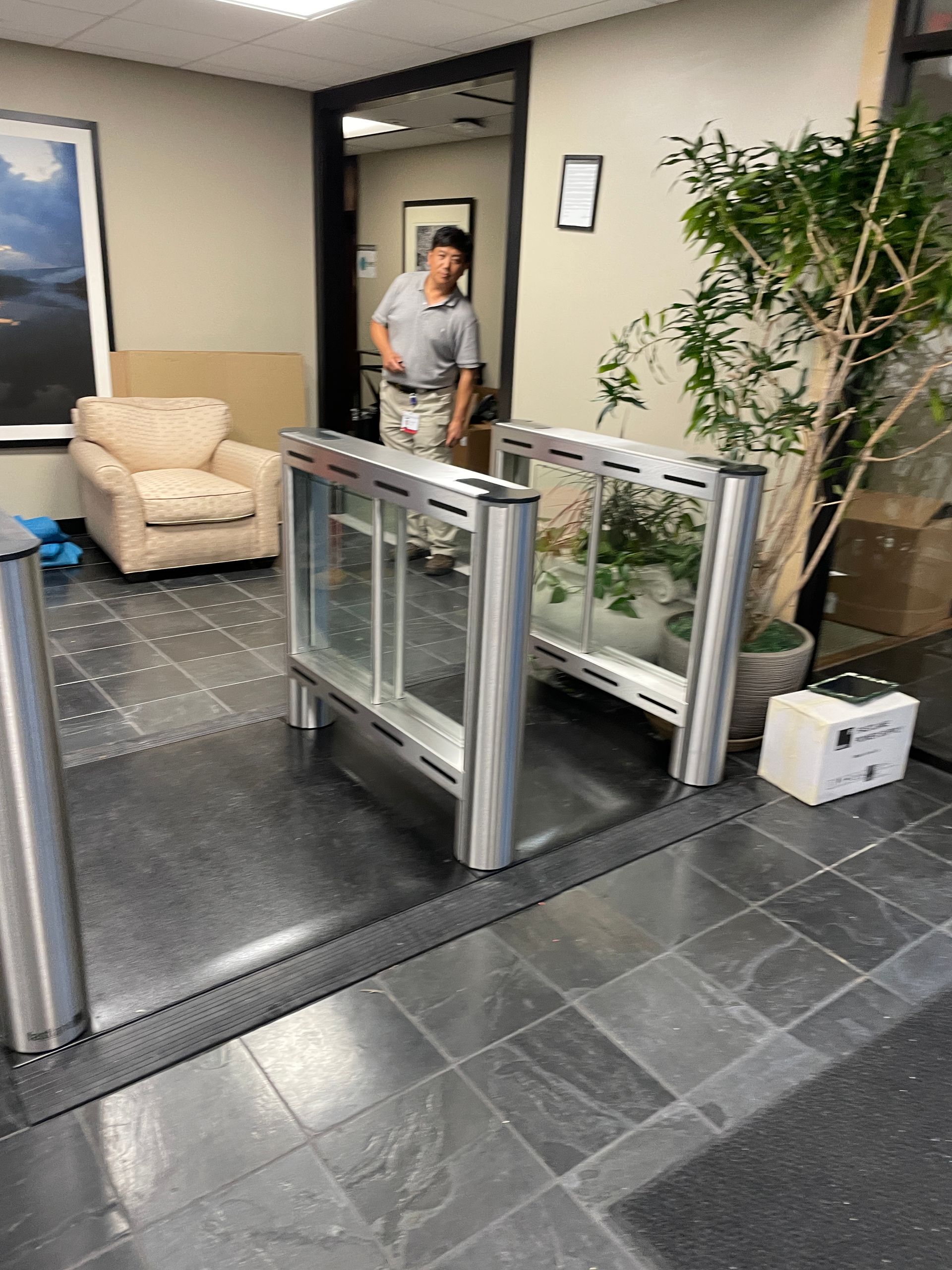 A security turnstile in an office building entrance, with a man standing in the doorway.