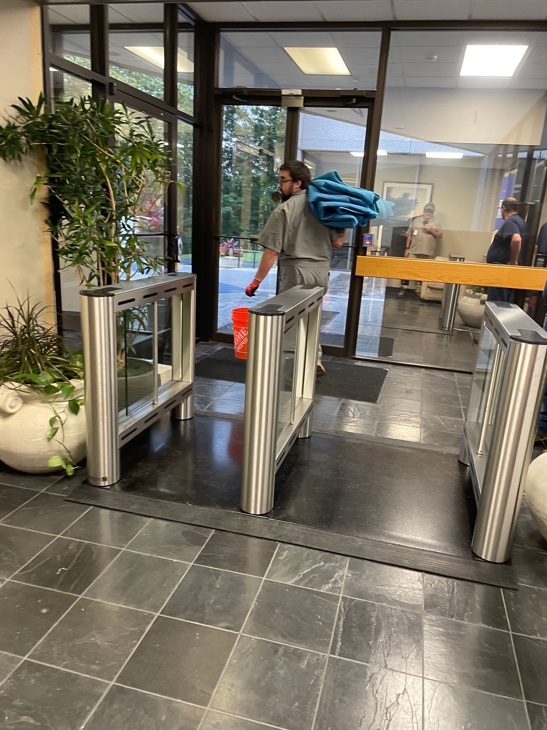 Man carrying items walks through security turnstile into an office building.