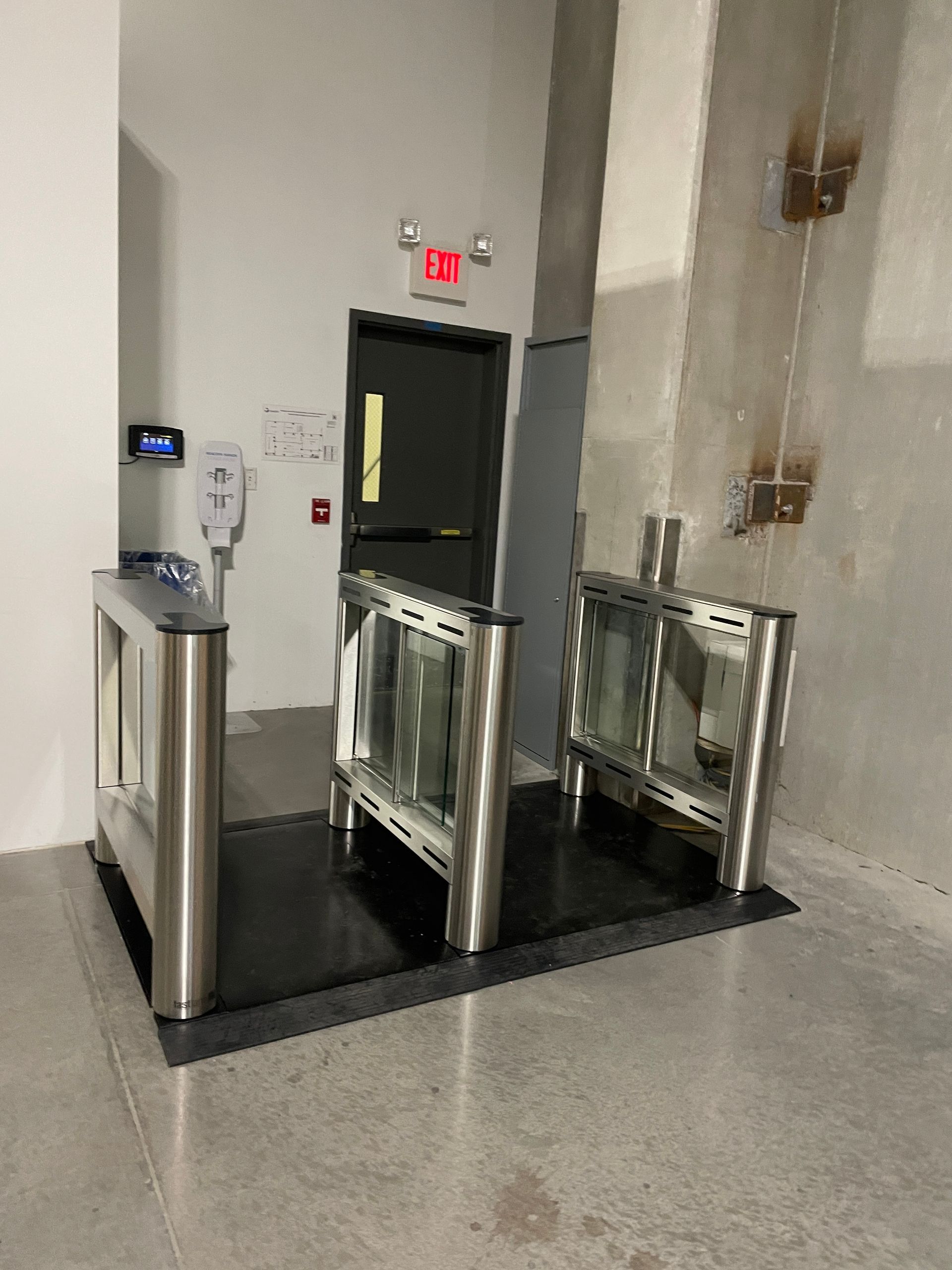Entrance with security turnstiles, a door, and an exit sign.