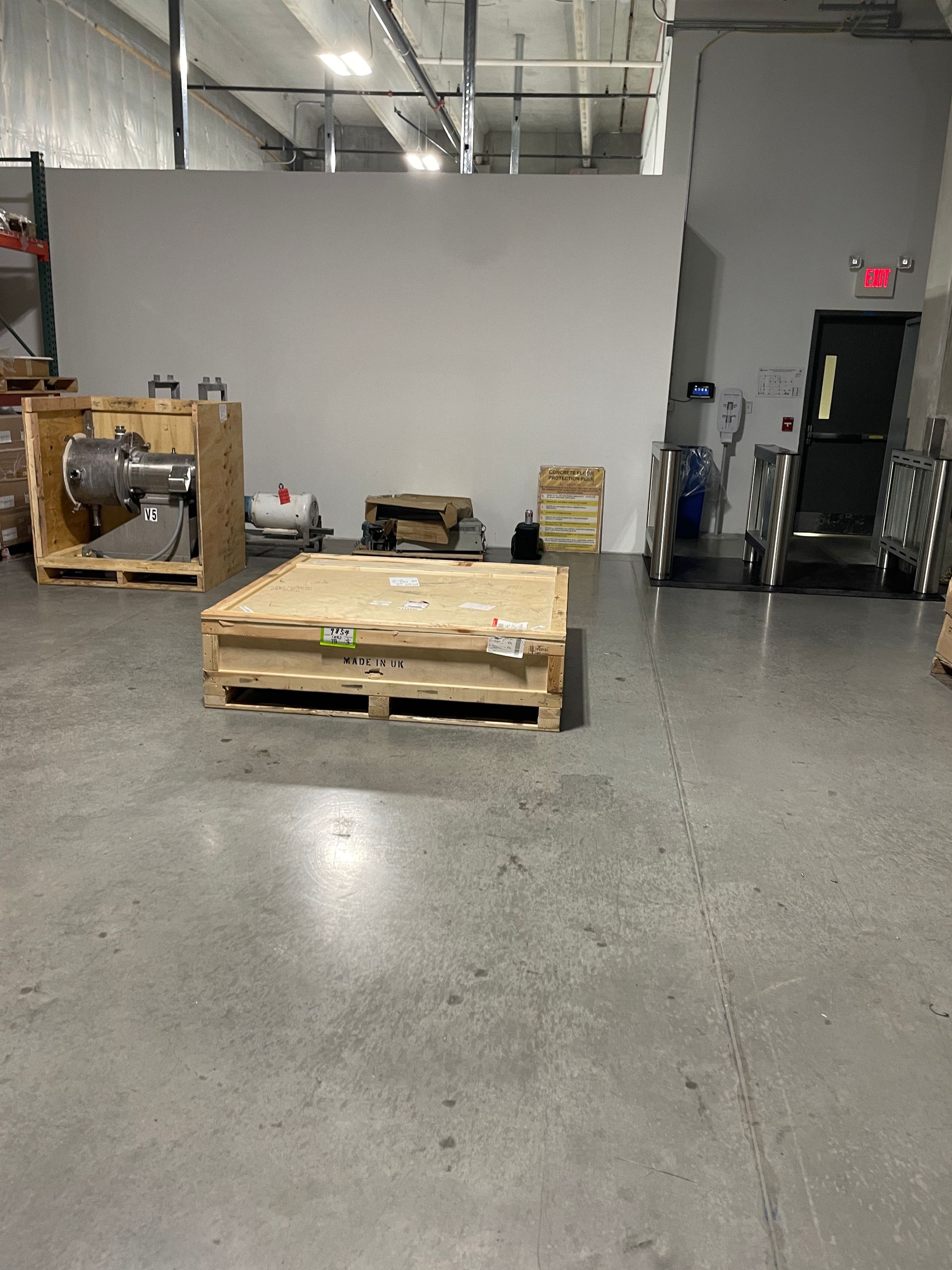 Warehouse interior with wooden crates, equipment, and a pallet on a gray concrete floor.