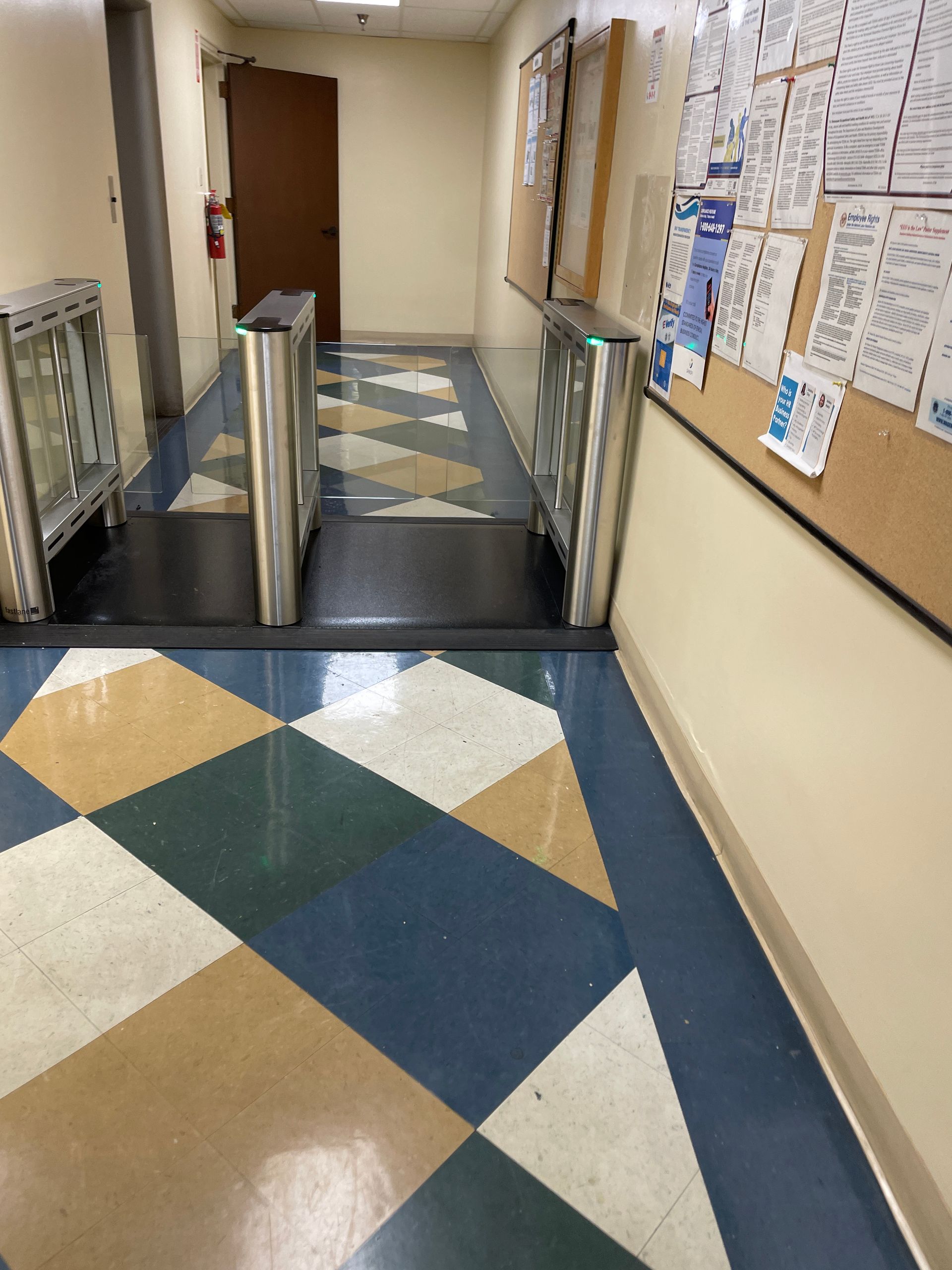 Hallway with turnstiles, bulletin board, and patterned floor.