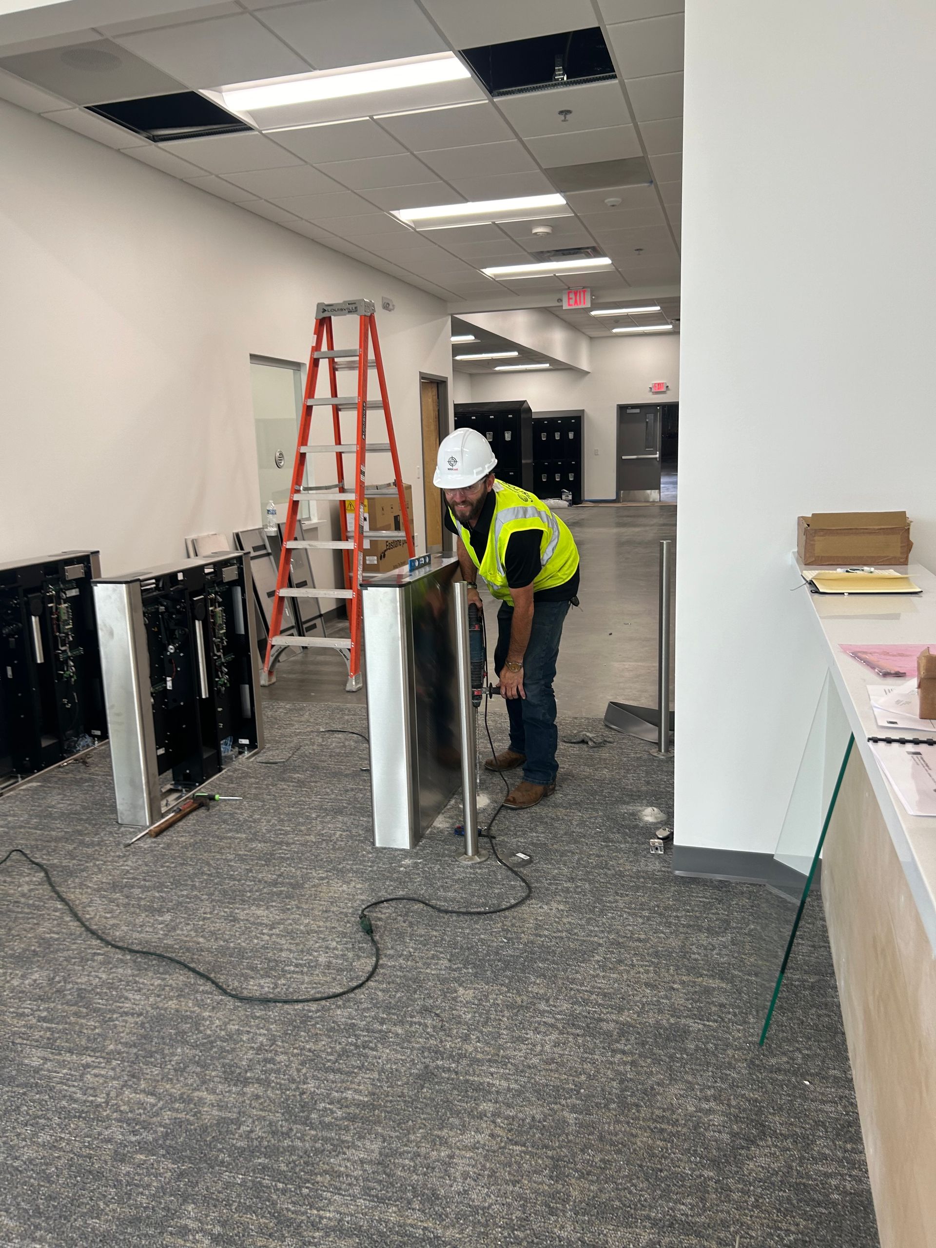 Construction worker in vest and hard hat working on metal panel in hallway.