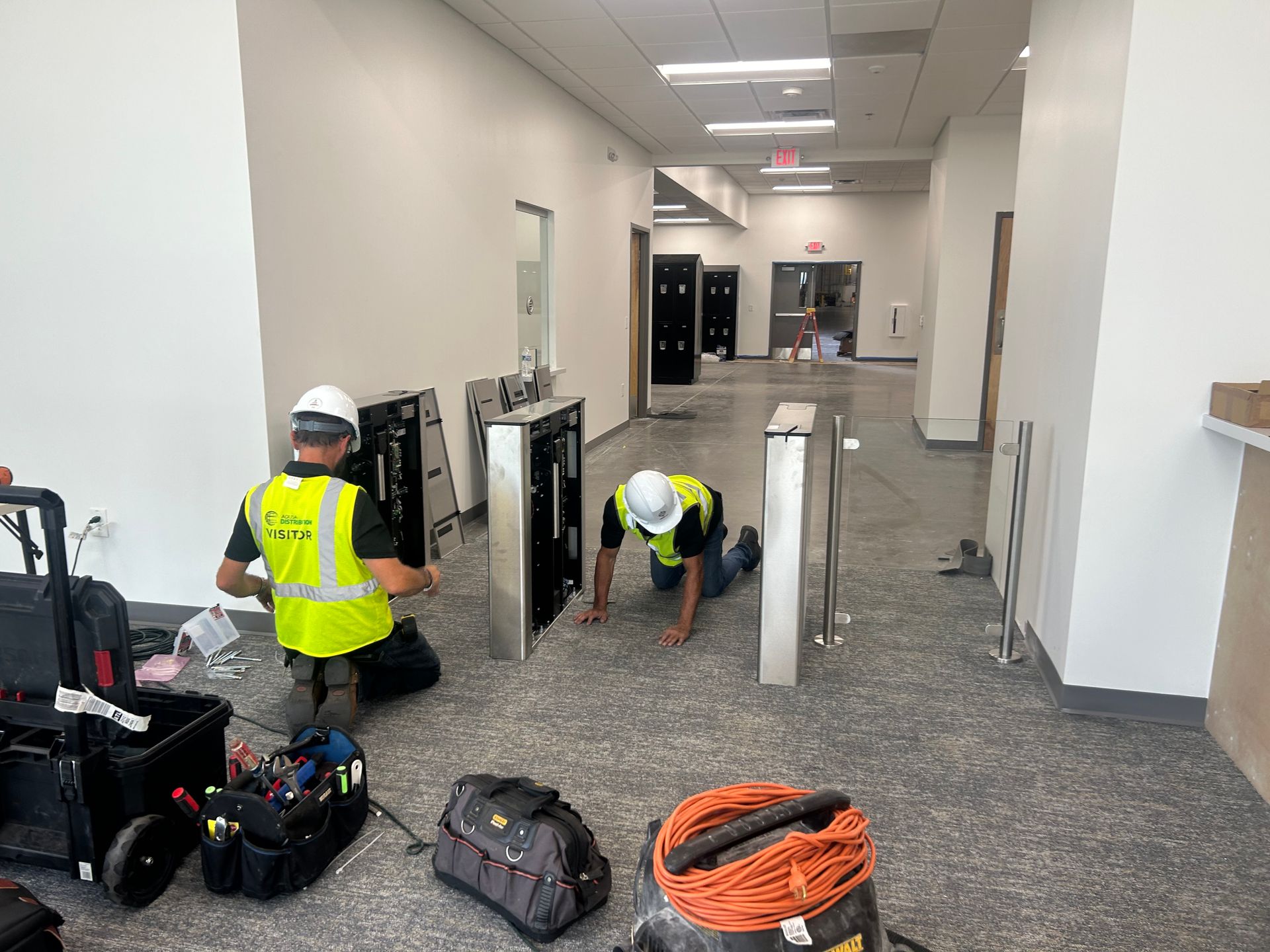 Two workers install security turnstiles in an office hallway. 