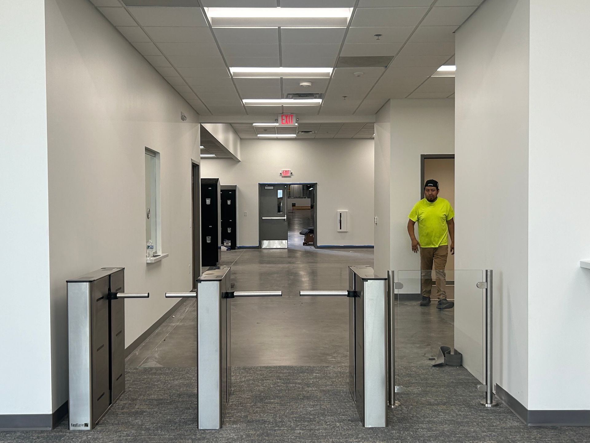 Hallway with turnstiles, a worker in yellow shirt, and doors.