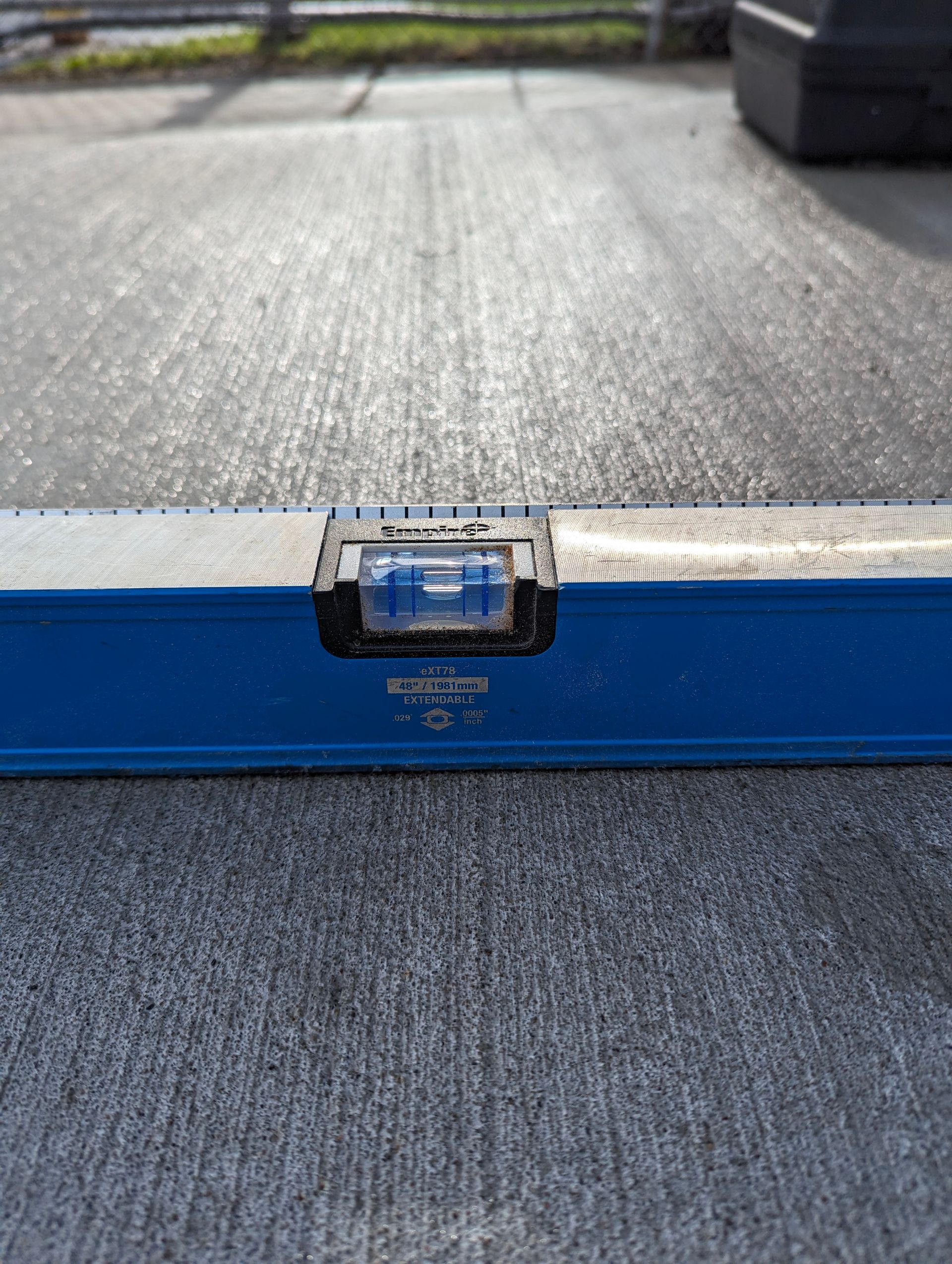 Blue level on gray concrete, bubble centered, indicating a level surface.