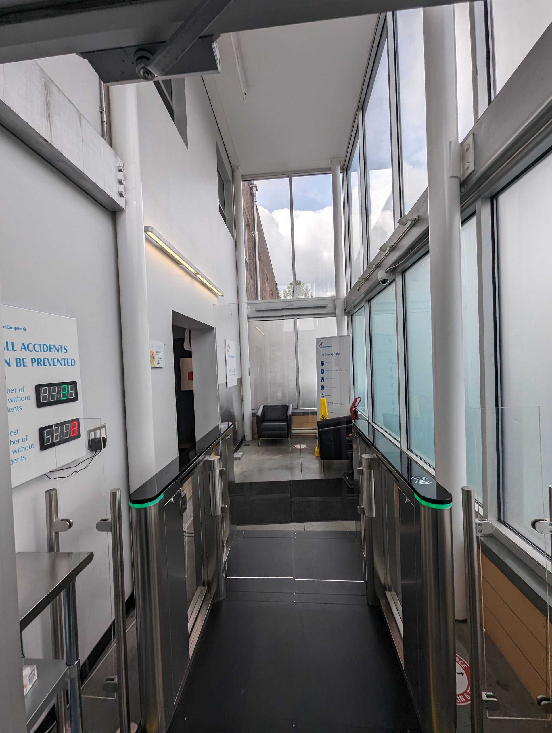 A narrow, glass-walled passageway with security turnstiles. 