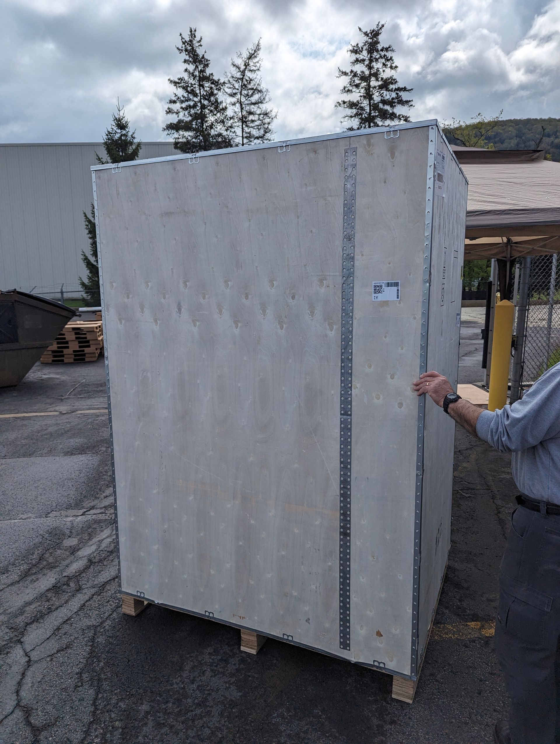 Large gray concrete panel on a wooden pallet; a person measures the side. Outdoors.