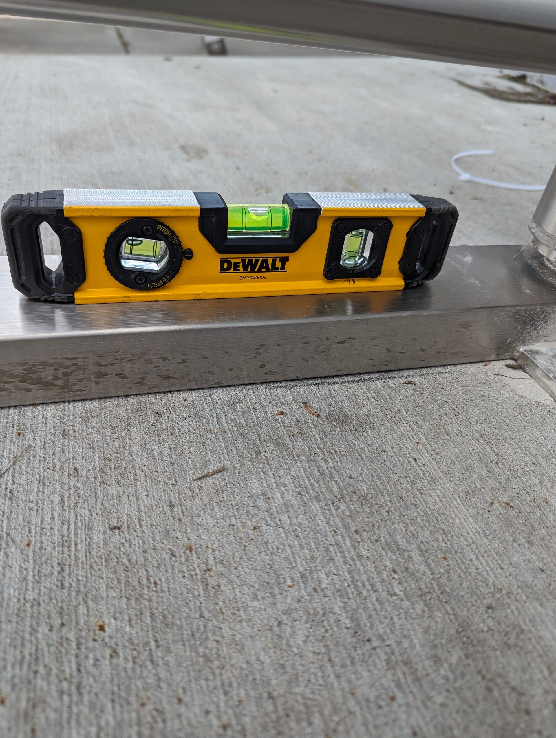Yellow DeWalt level on a gray metal surface, bubble centered, showing a level measurement.