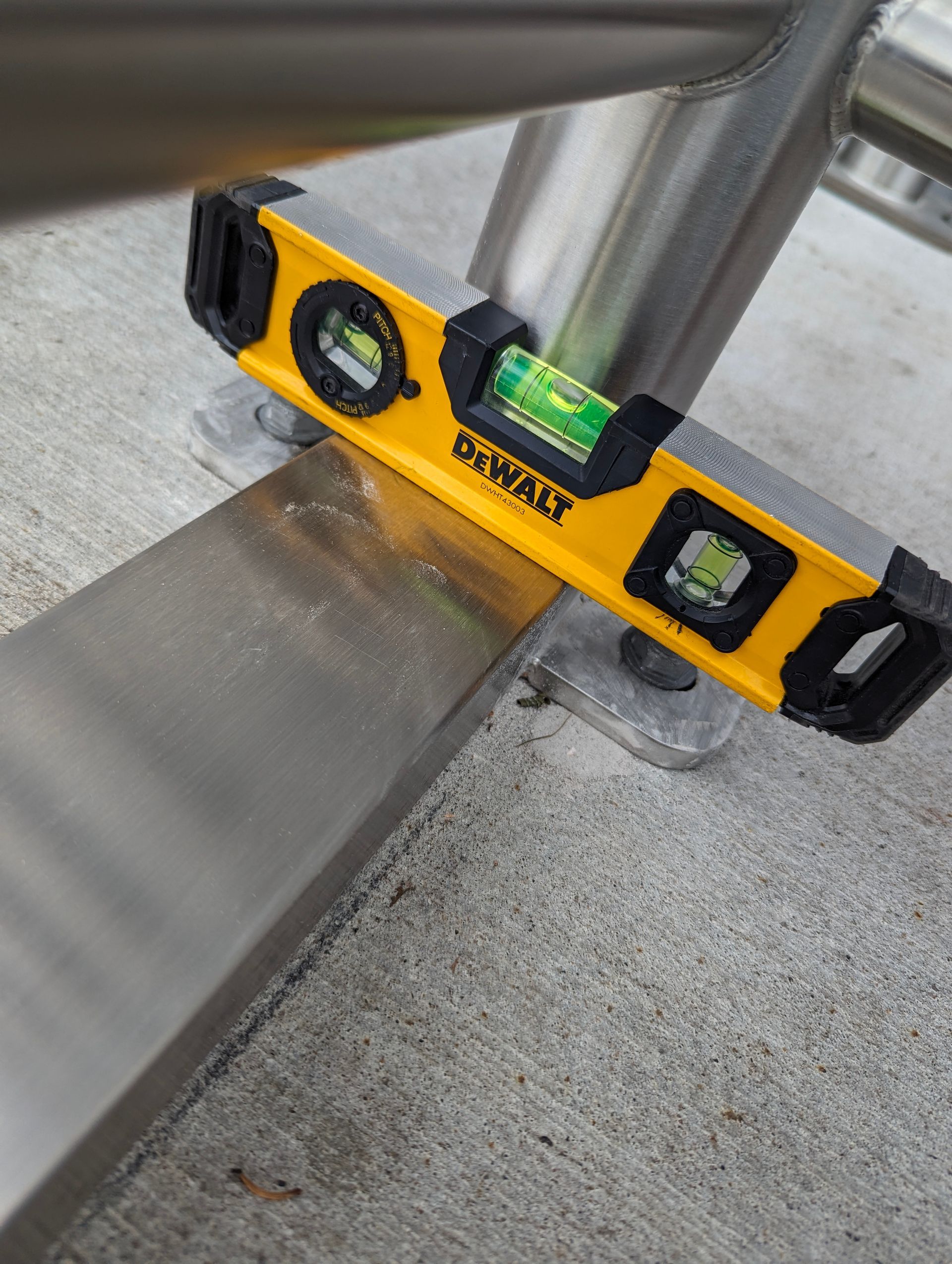 A yellow level rests on a metal bar attached to a railing, checking for levelness on a concrete surface.