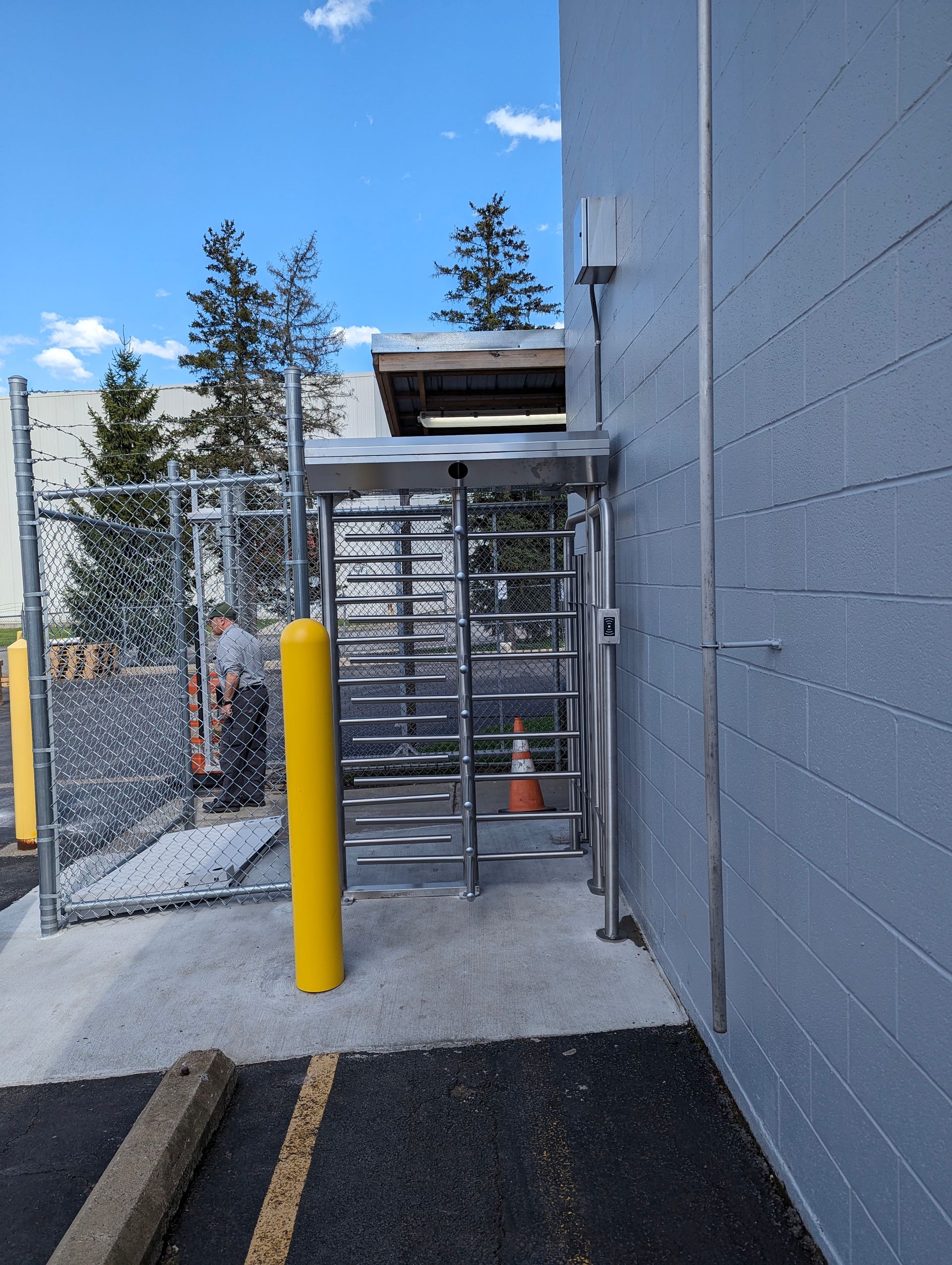 Turnstile security entrance next to a gray building and chain-link fence.