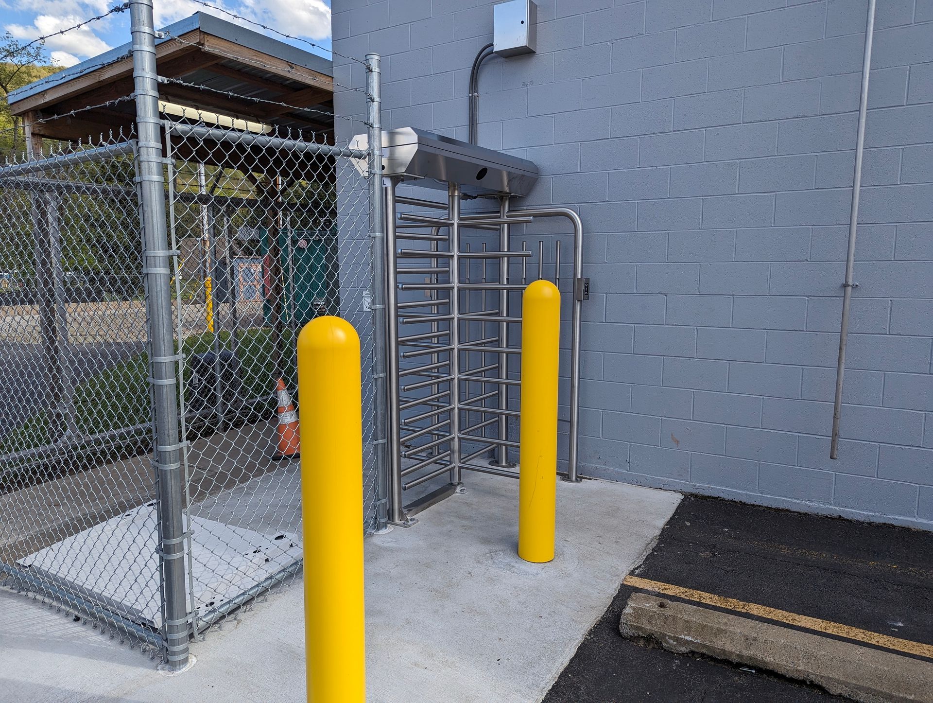 A turnstile entry point with yellow bollards and chain link fence.
