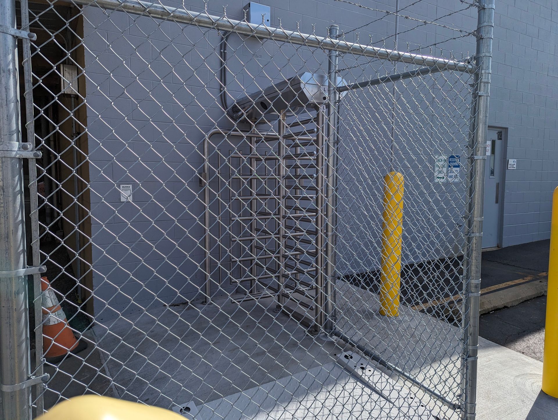 Chain-link fence encloses a turnstile entrance to a building. 