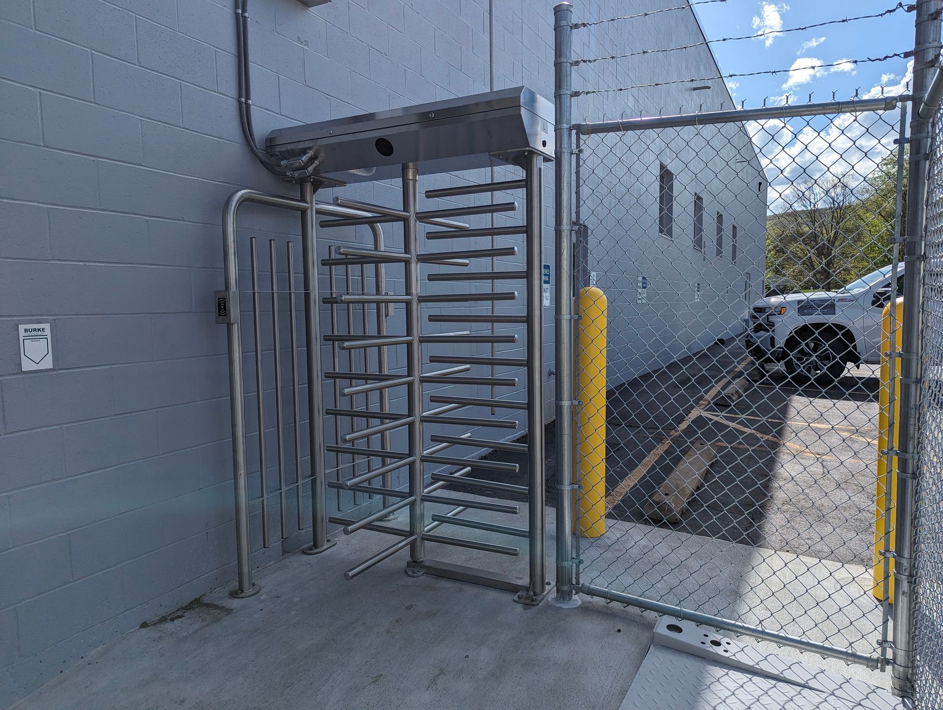 A metal turnstile entrance next to a chain-link fence, outside a building, in an industrial setting.
