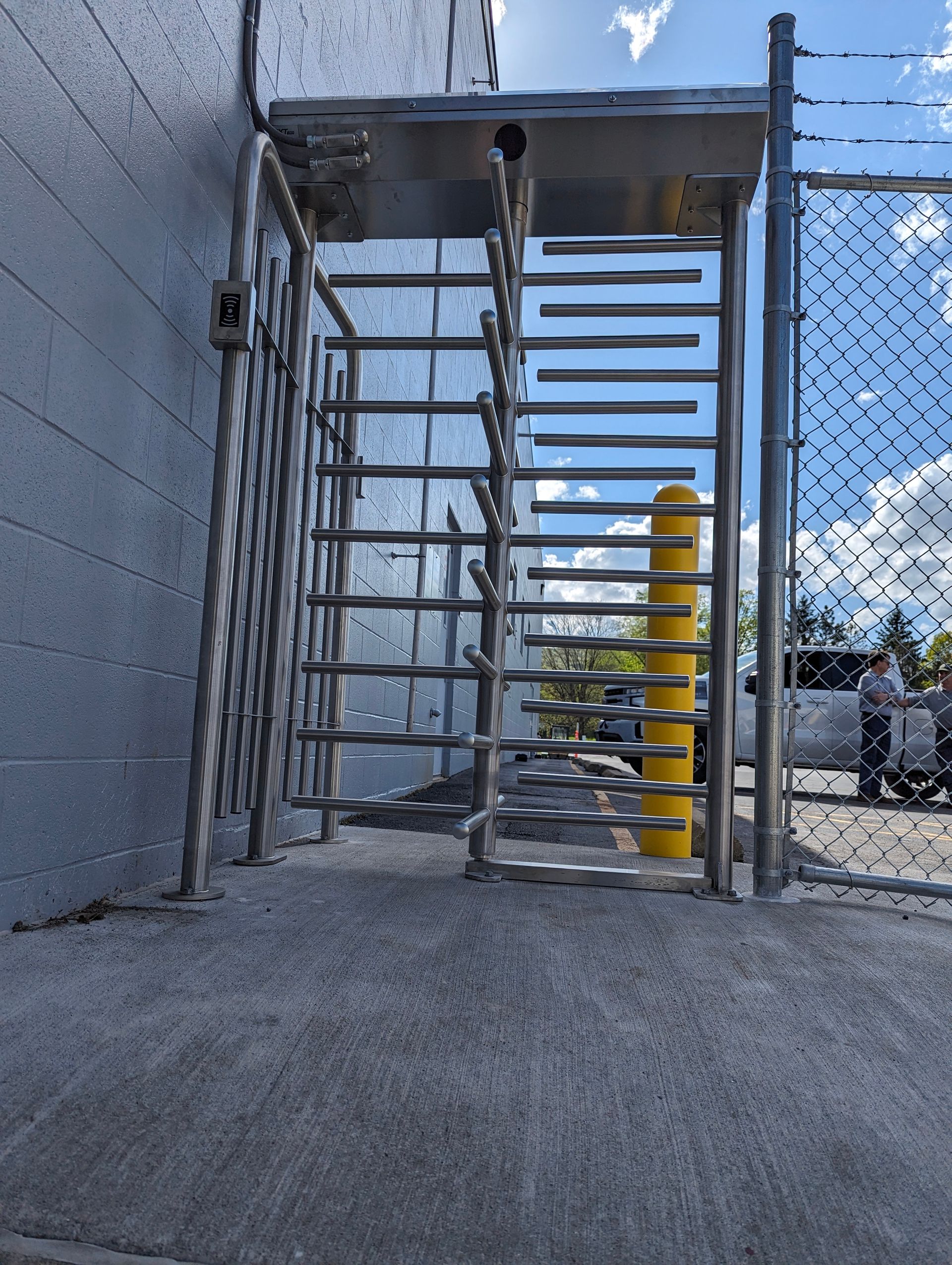 Turnstile entrance next to a concrete wall and chain-link fence.