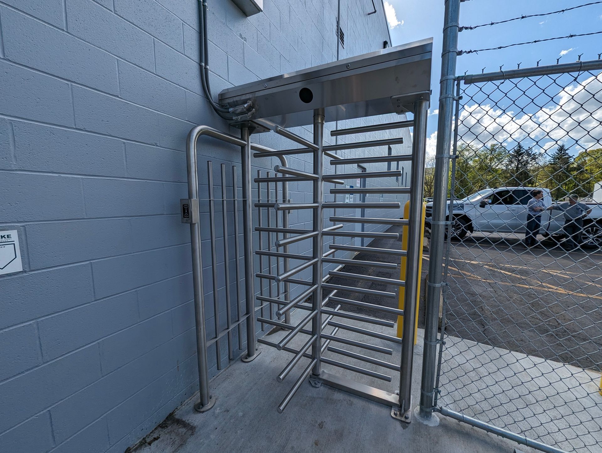 Turnstile at a gate, gray brick building background, truck in view.