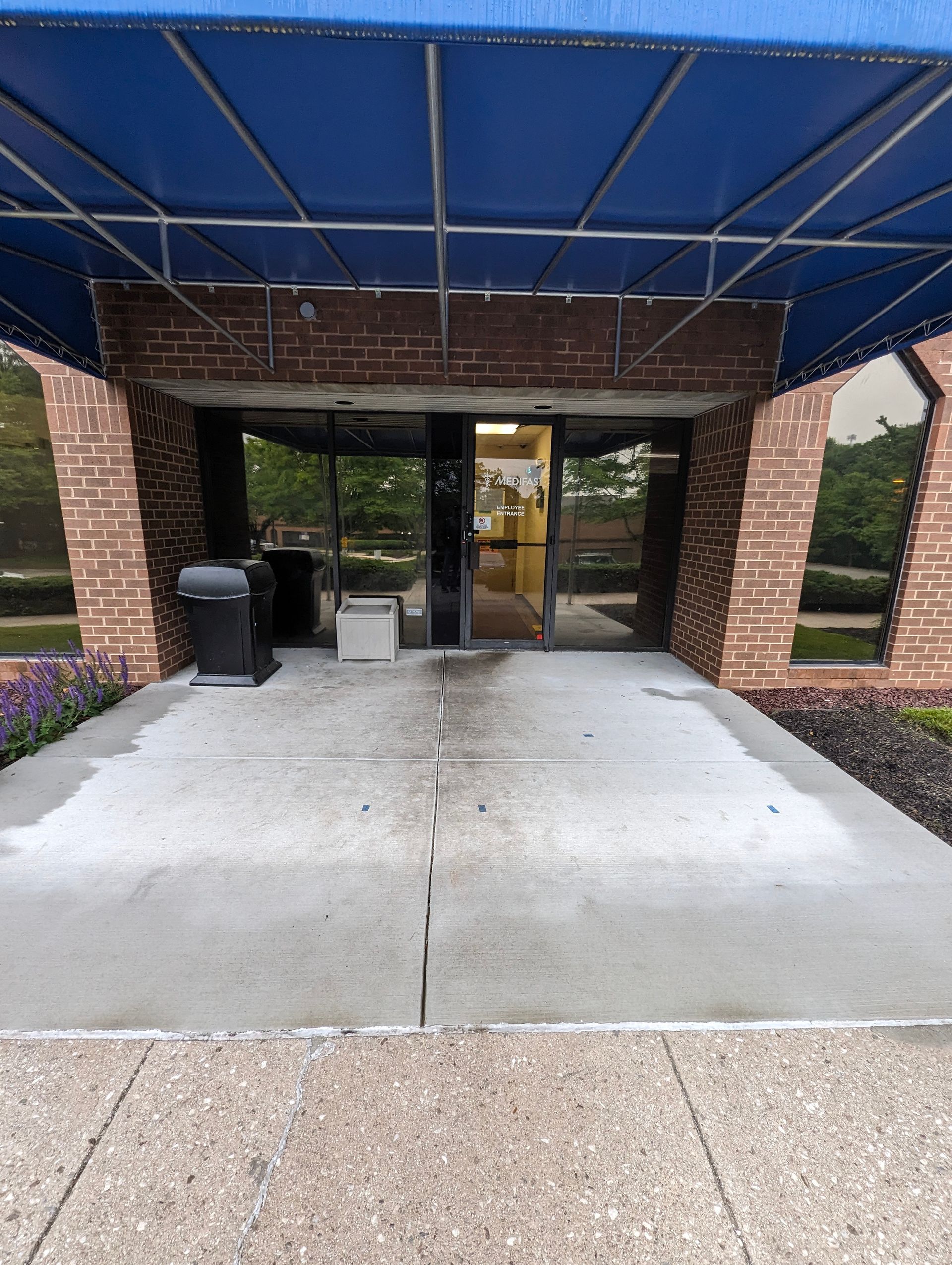 Entrance to a building with glass doors, brick walls, a blue canopy, and concrete walkway.