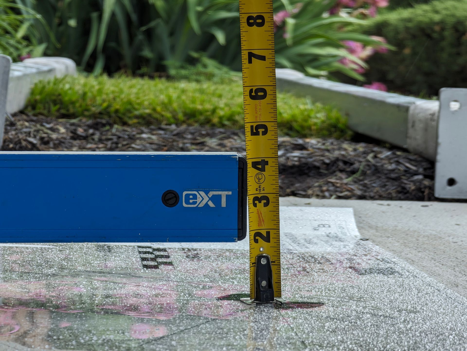 A level and tape measure resting on a concrete surface, measuring its height. 