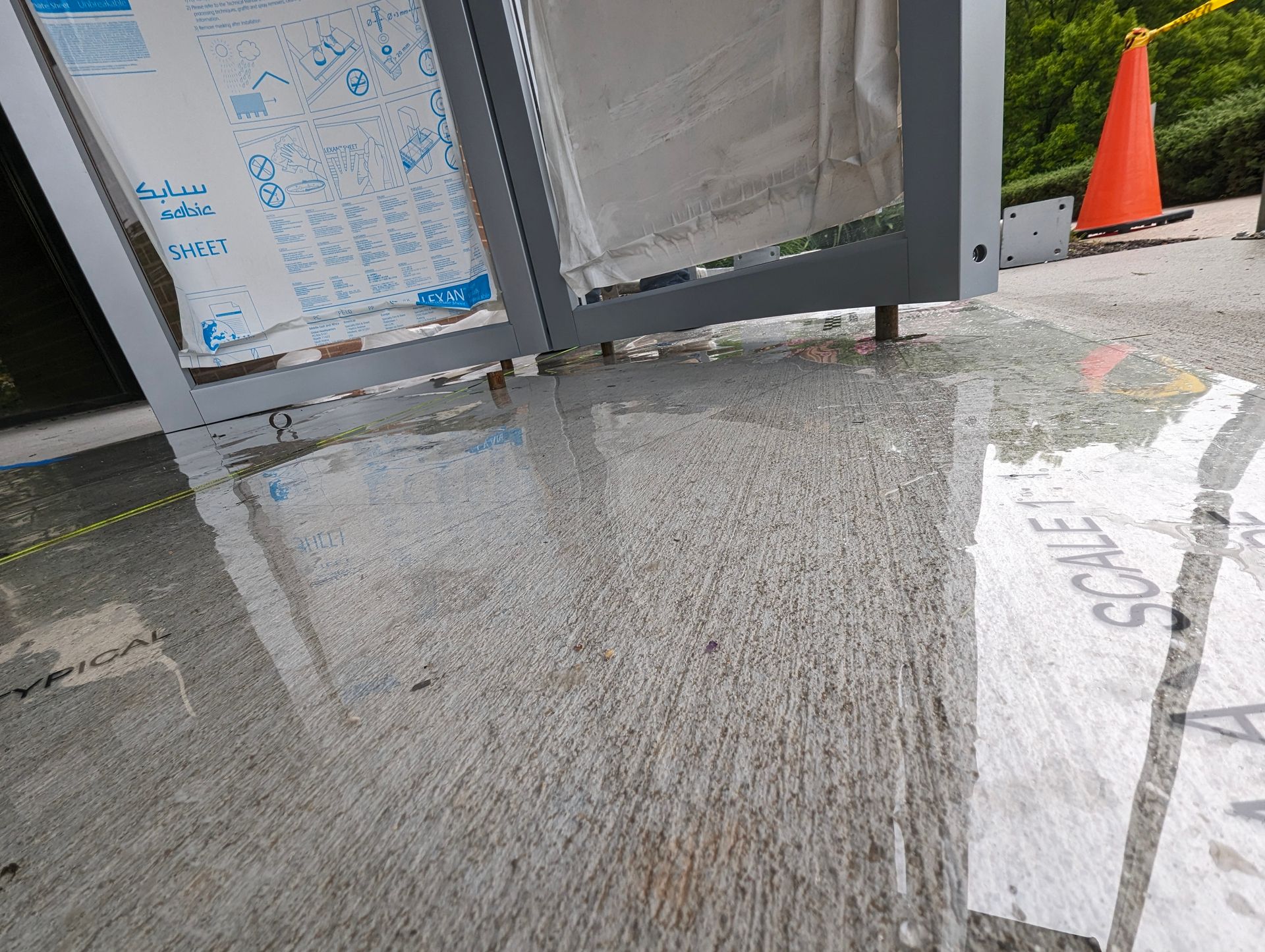 Water puddles on a concrete surface under a silver-framed structure.