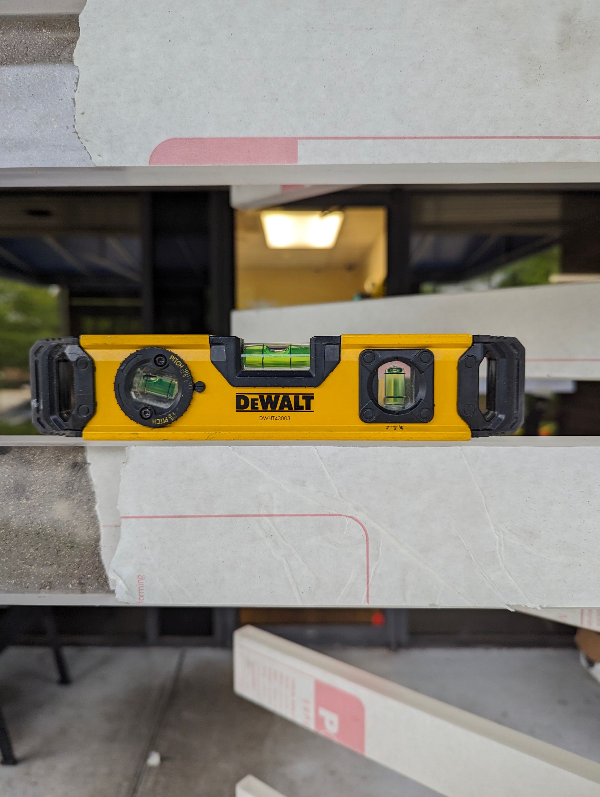 Yellow DeWalt level on white construction material, showing a level reading. 