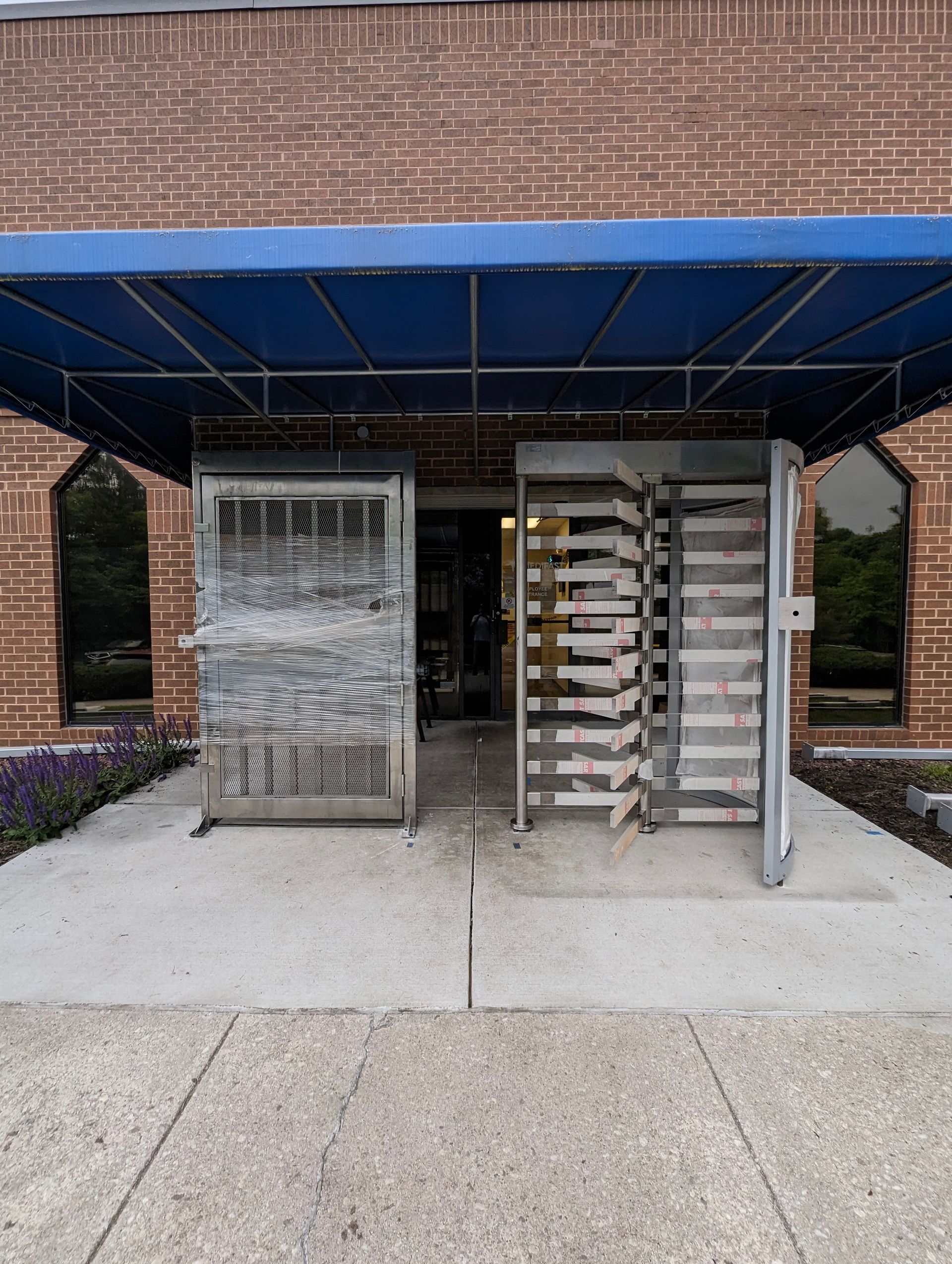 Entrance with a blue awning, turnstiles, and a weathered gate in front of a brick building. 
