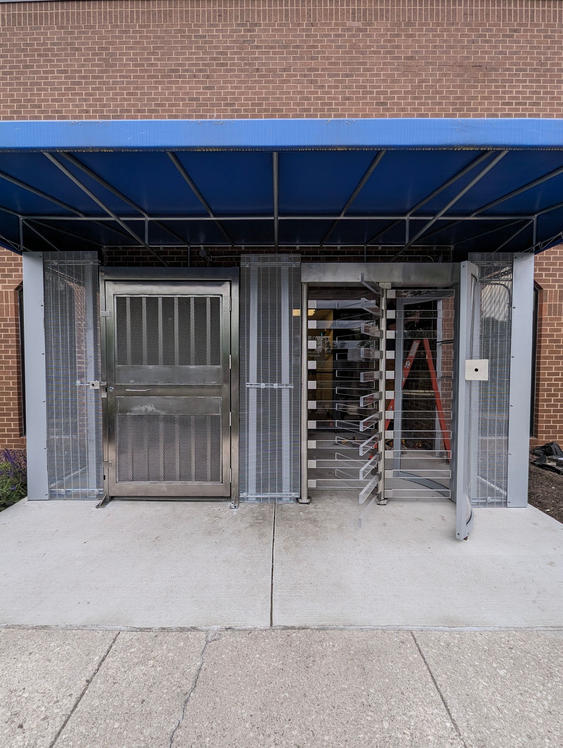 Building entrance with blue awning, stainless steel doors and a revolving door. 