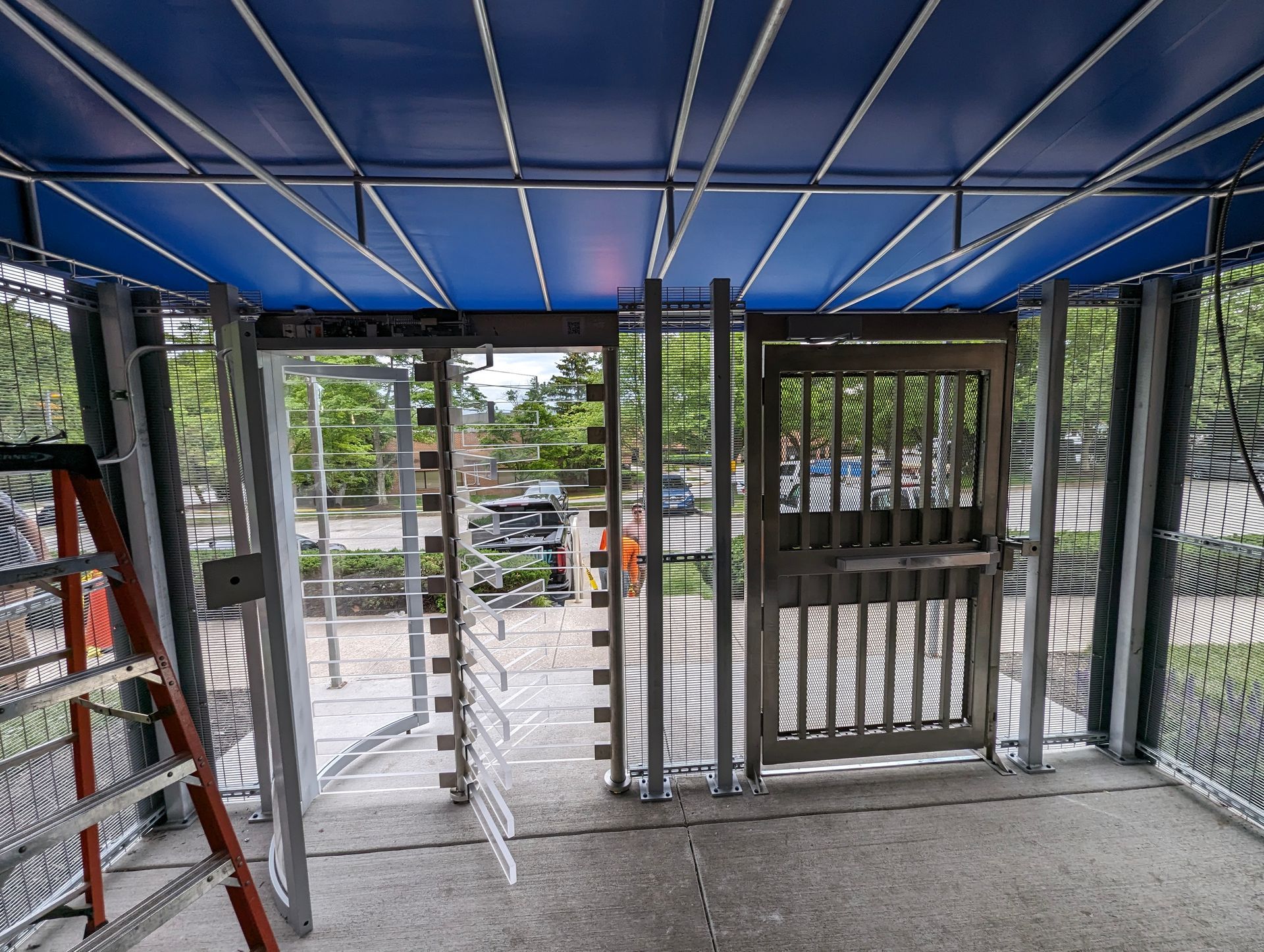 Metal framed structure with blue ceiling, doors, and wire mesh walls. 