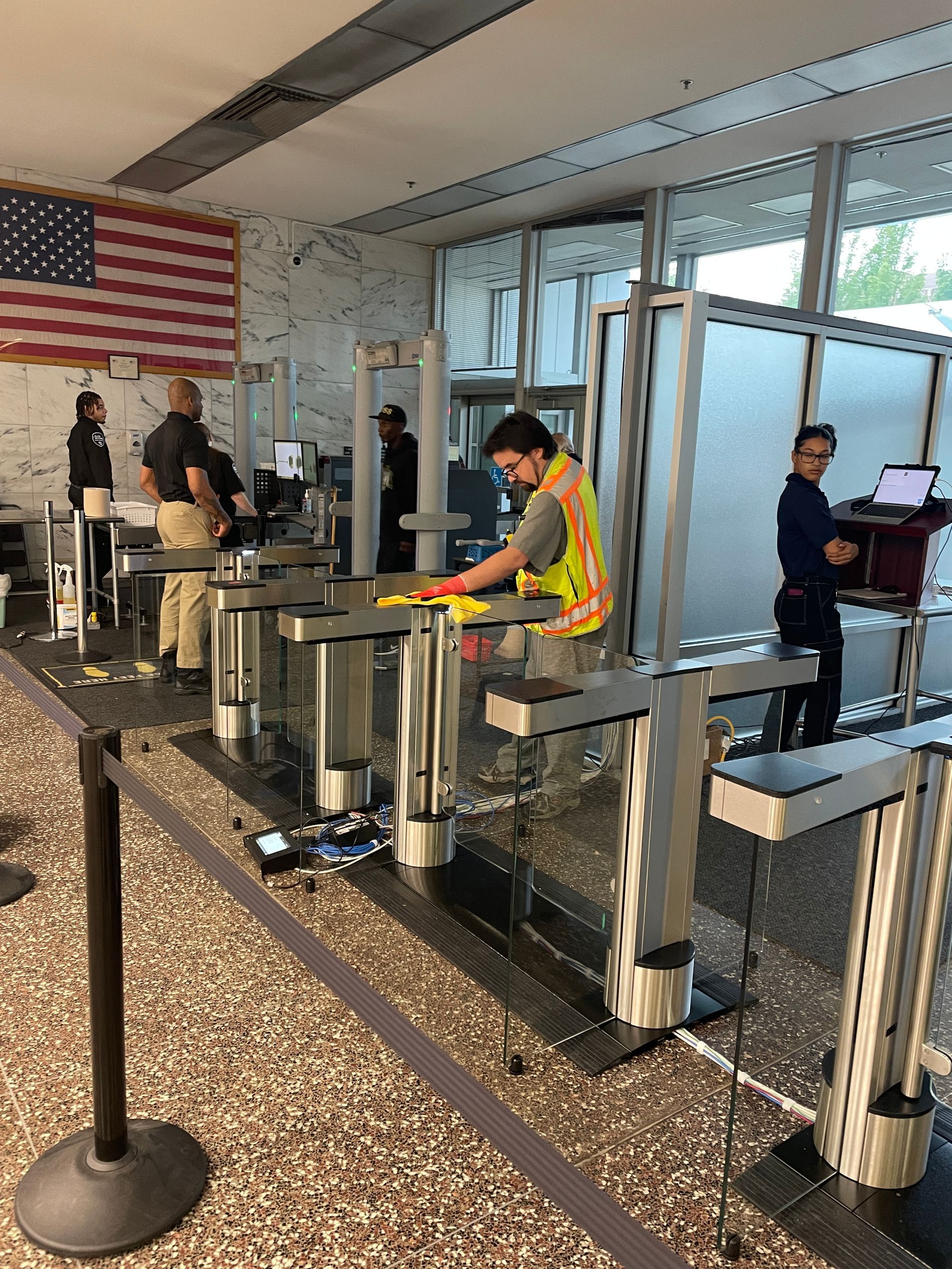 Worker in safety vest cleans, others stand behind security gates.