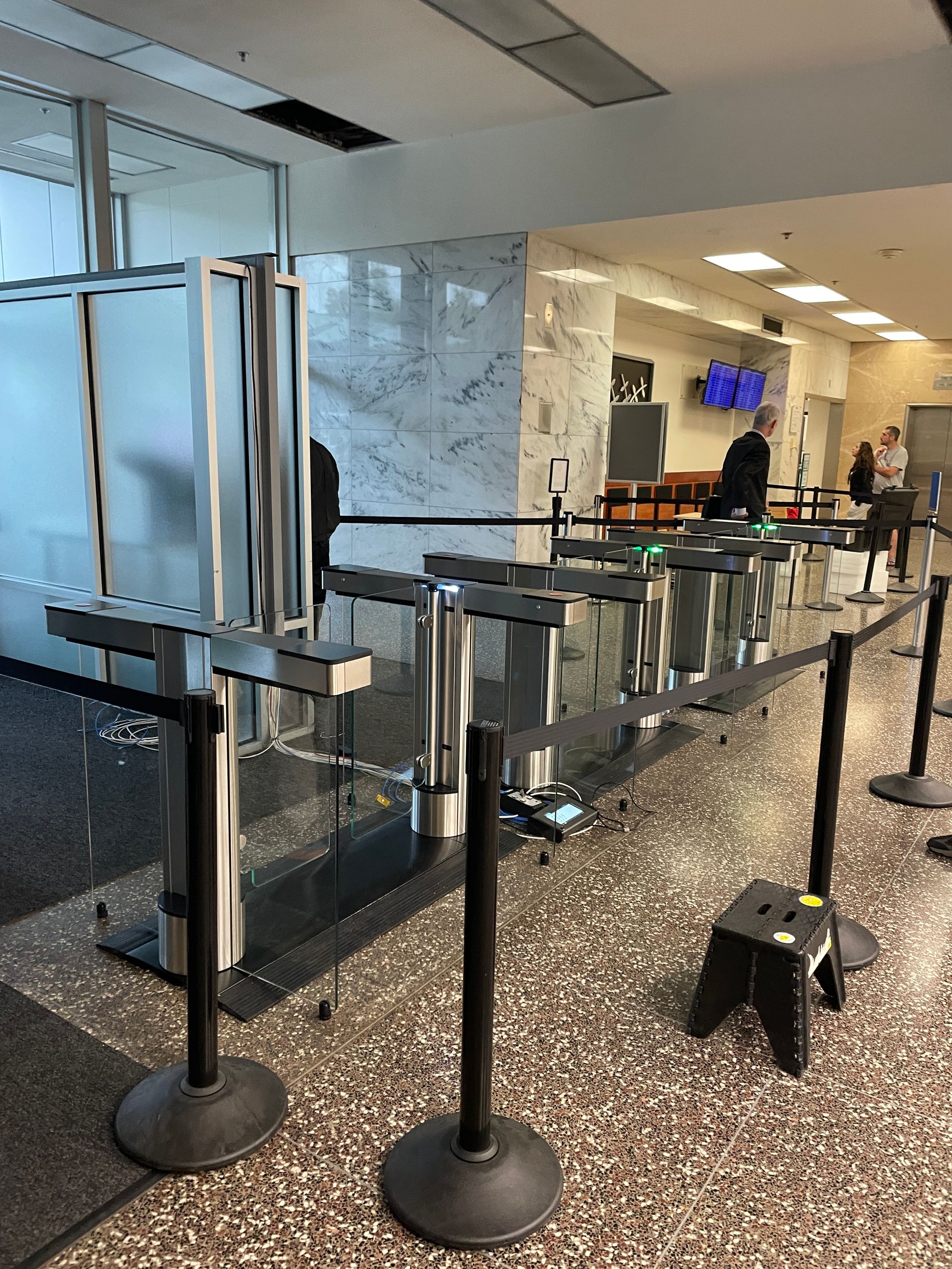 A security checkpoint with stanchions and a line in a building lobby.
