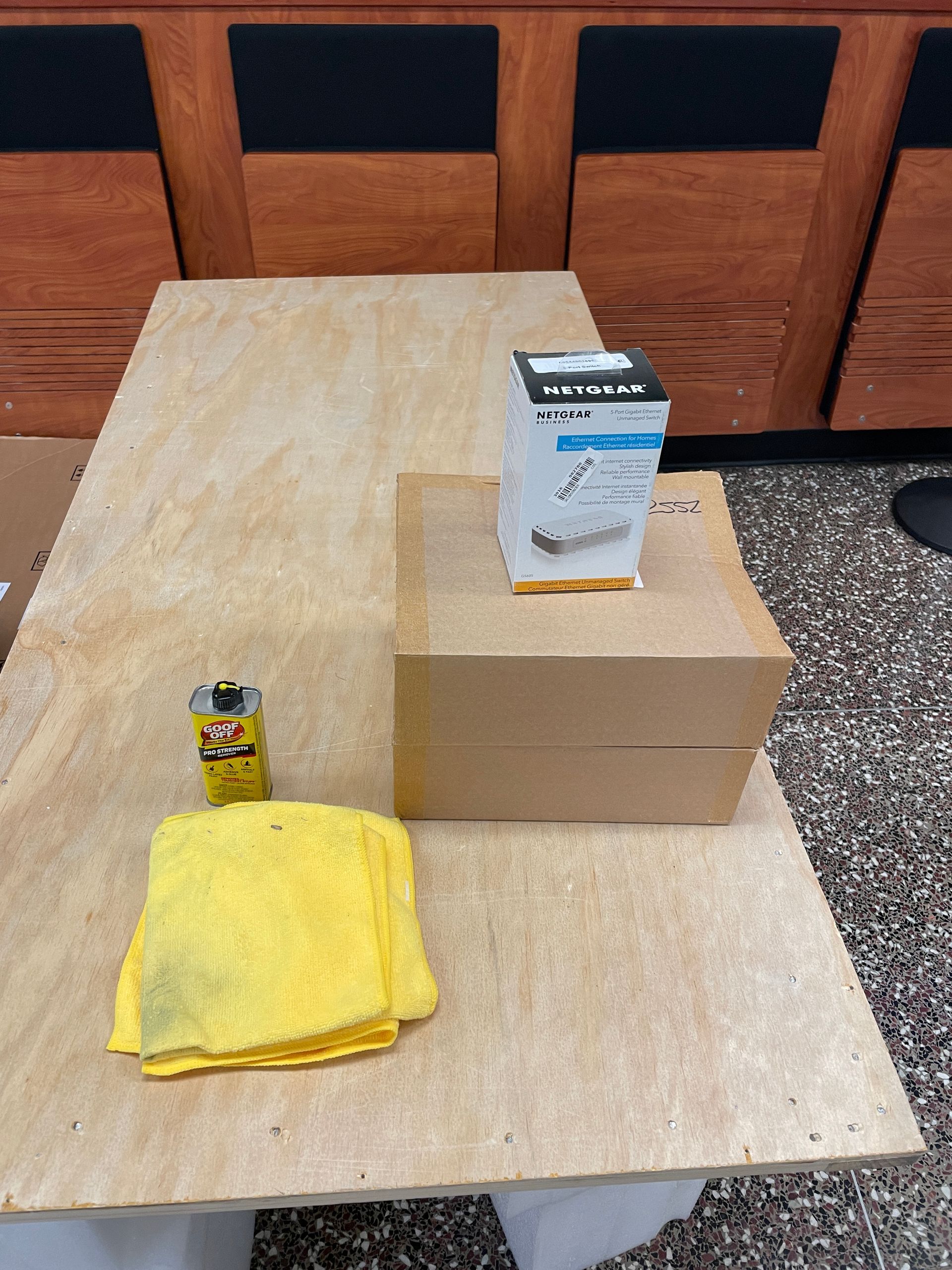 A power strip box, a battery, and a yellow cloth sit on a plywood surface.