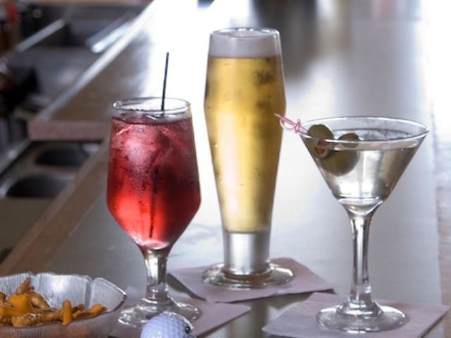 Three drinks are on a bar including a martini and a beer