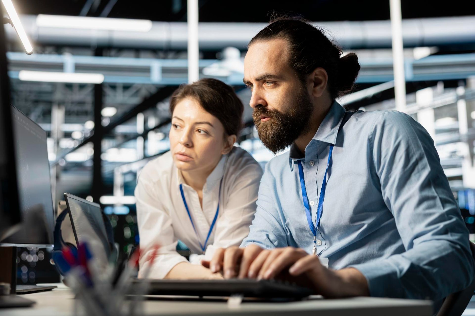 Man and woman looking at a computer screen in a tech facility, both wearing lanyards.