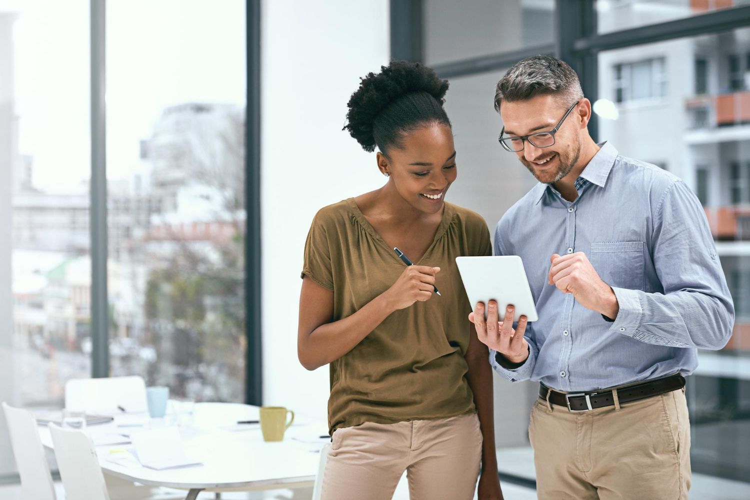 Two people, looking at a tablet, in an office. One points with a pen, the other smiles.