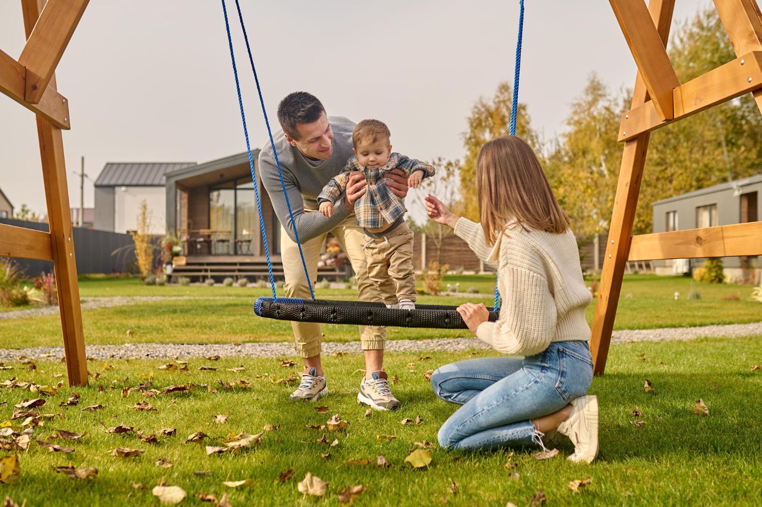 Family helping a toddler onto a swing in a grassy yard.