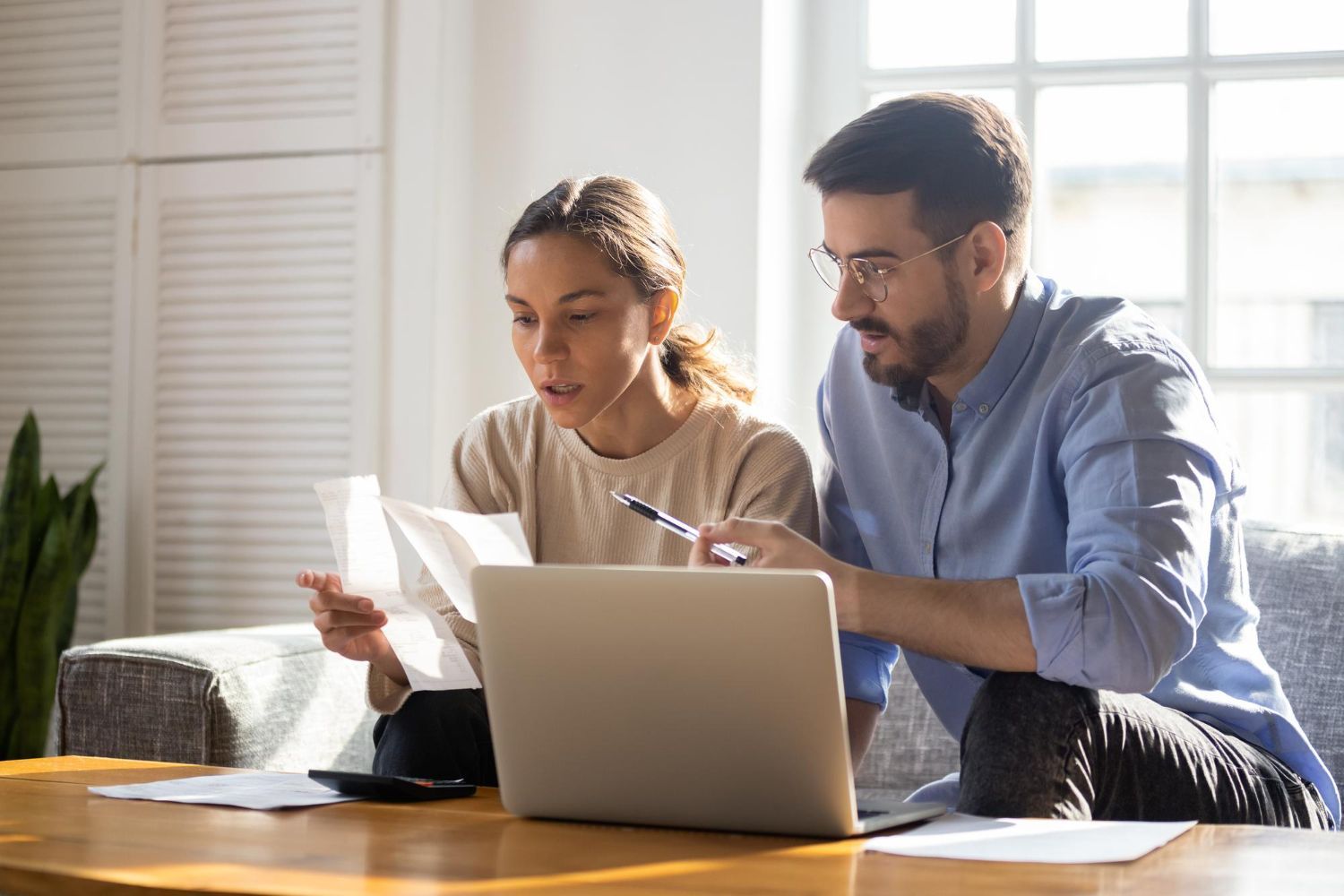 Couple reviewing documents with a laptop on a table in a home setting.