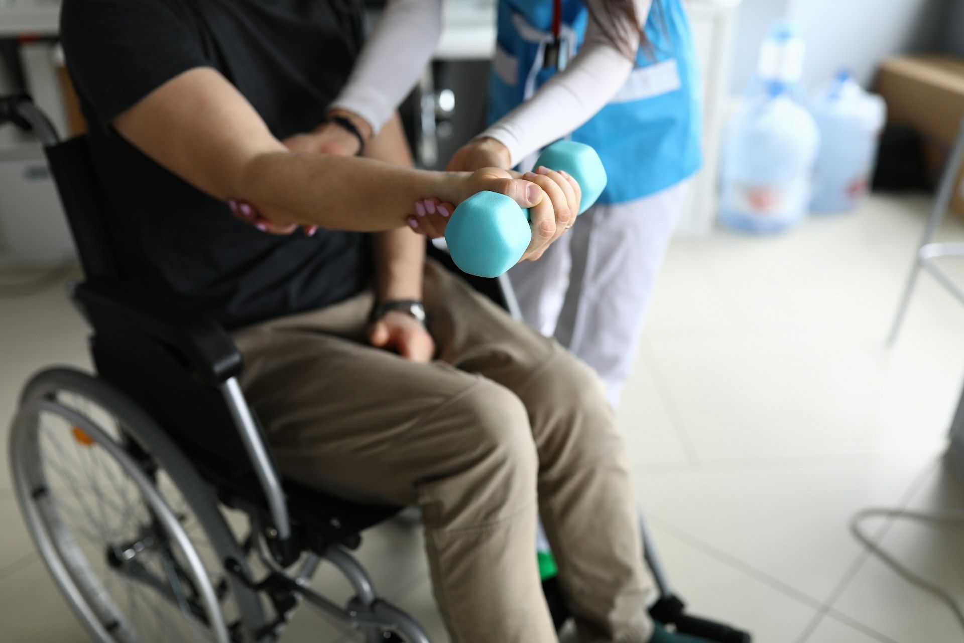 Person in wheelchair doing arm exercise with dumbbell, assisted by caregiver.