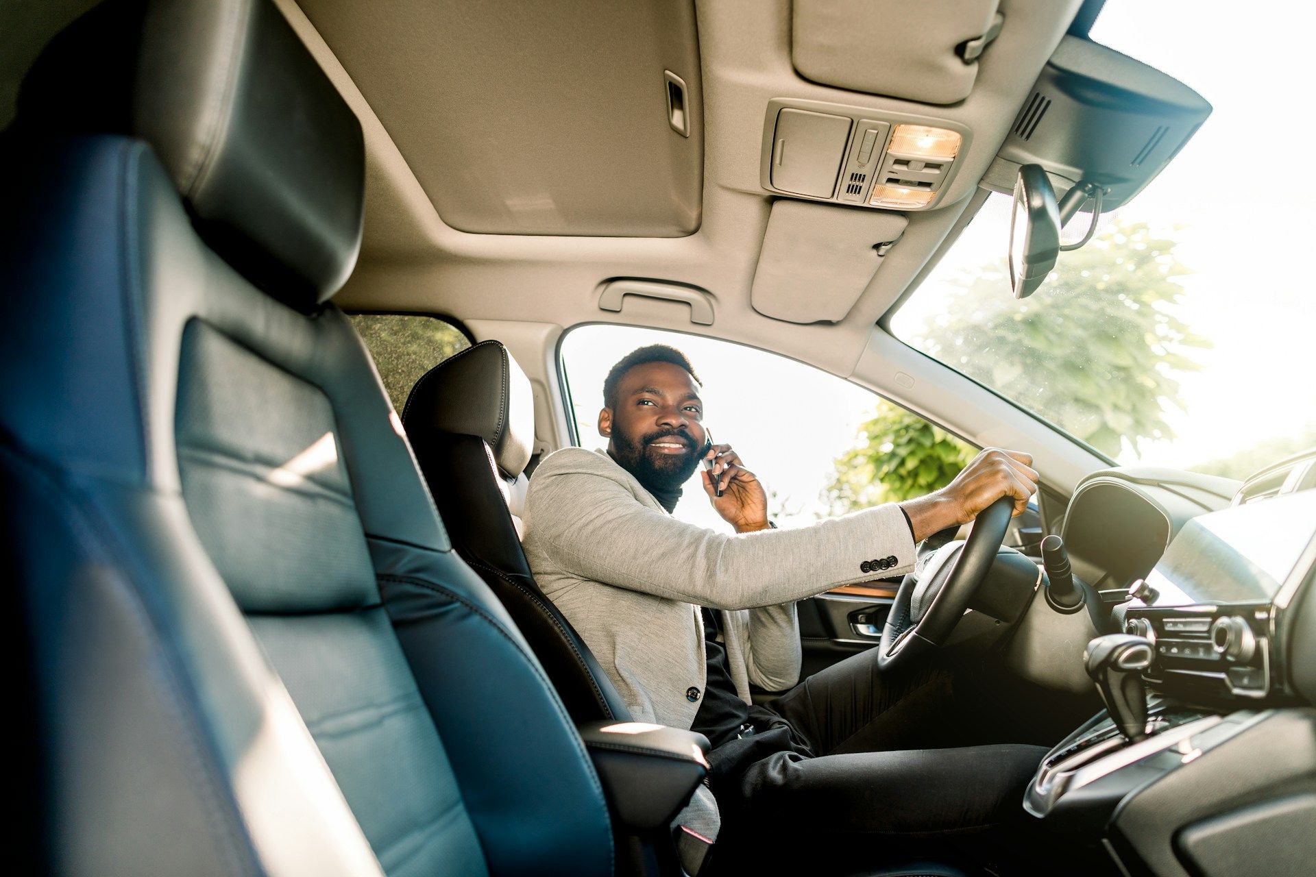 Man in a car, smiling while on a phone. Sunlight visible.
