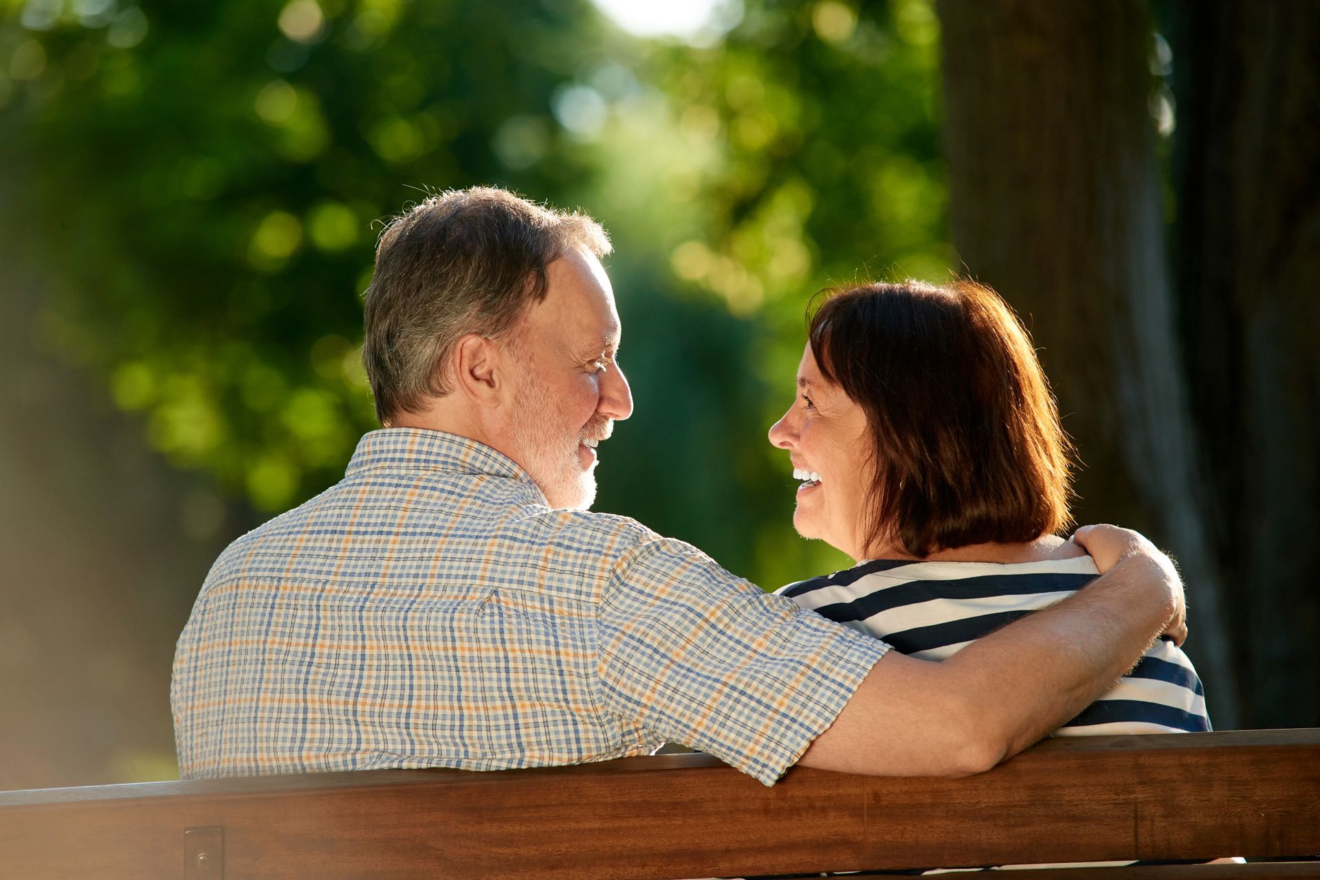 Man in gray blazer driving a car, smiling and talking on a phone. Sunlight visible.